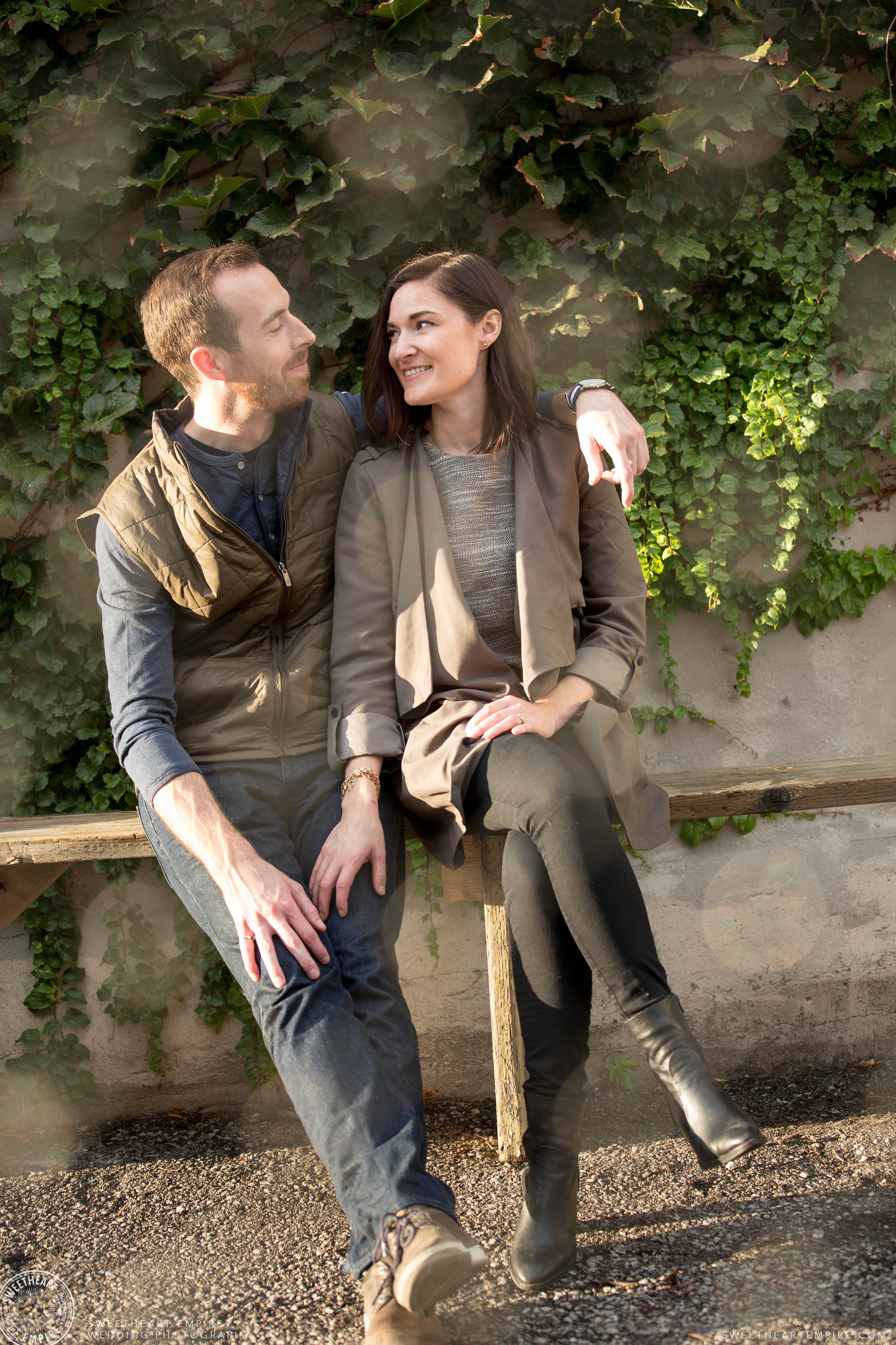 In-love couple looking at one another sitting in front of ivy wall, Leslieville engagement photos