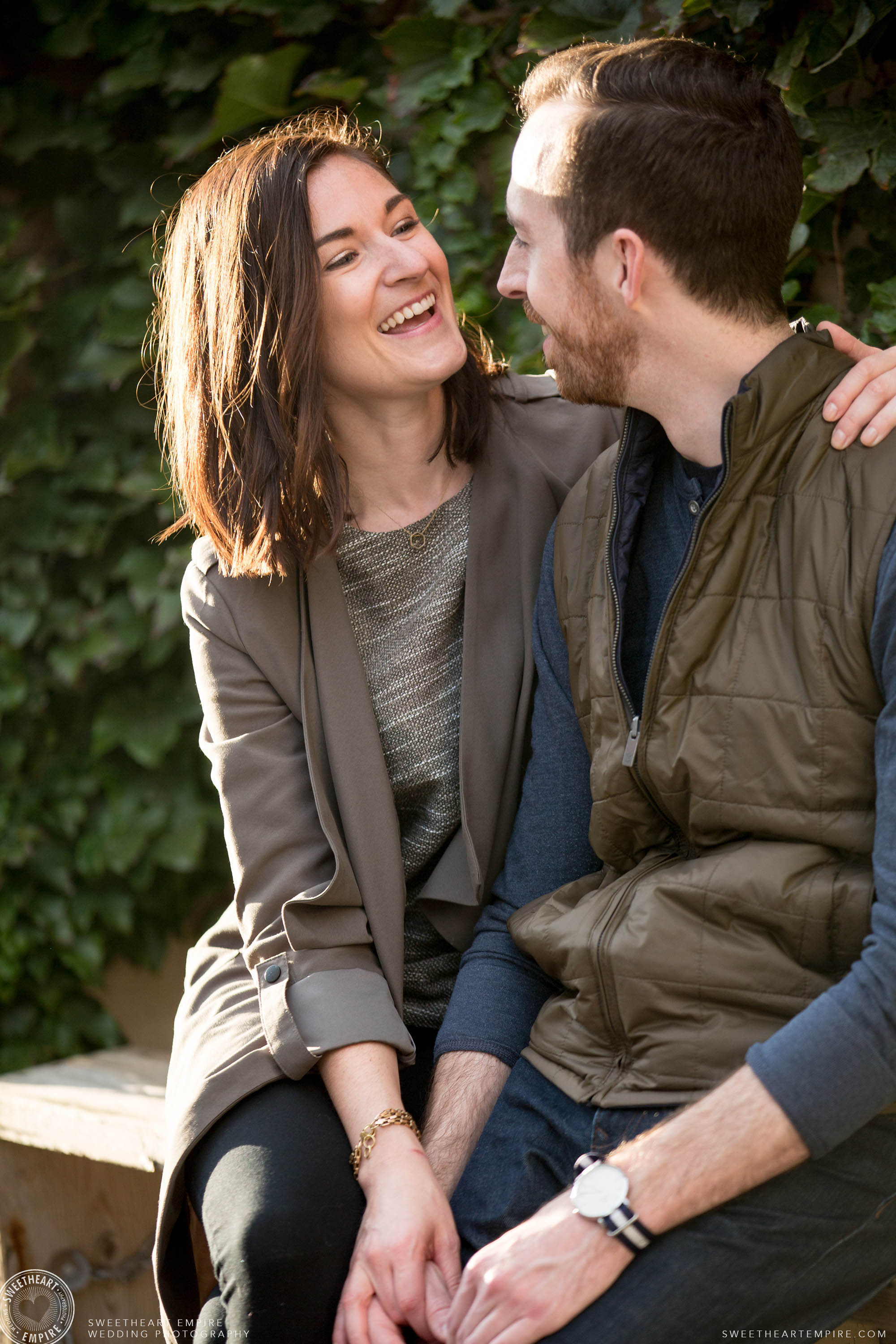 Happy couple laughing together in front of an ivy wall