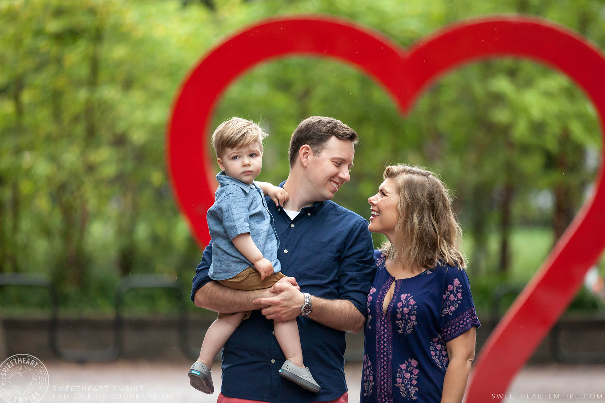 Mom and dad share a loving look while walking with son in front of oversized heart, Distillery District Family Photography