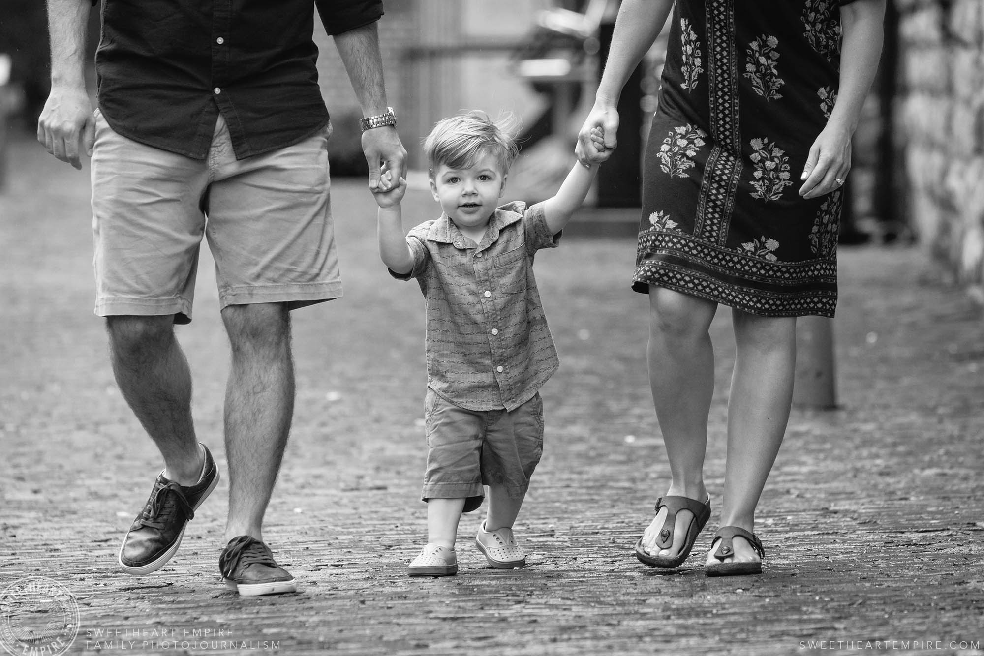 05_Sweet toddler holding his dad and moms hands in the distillery district.jpg