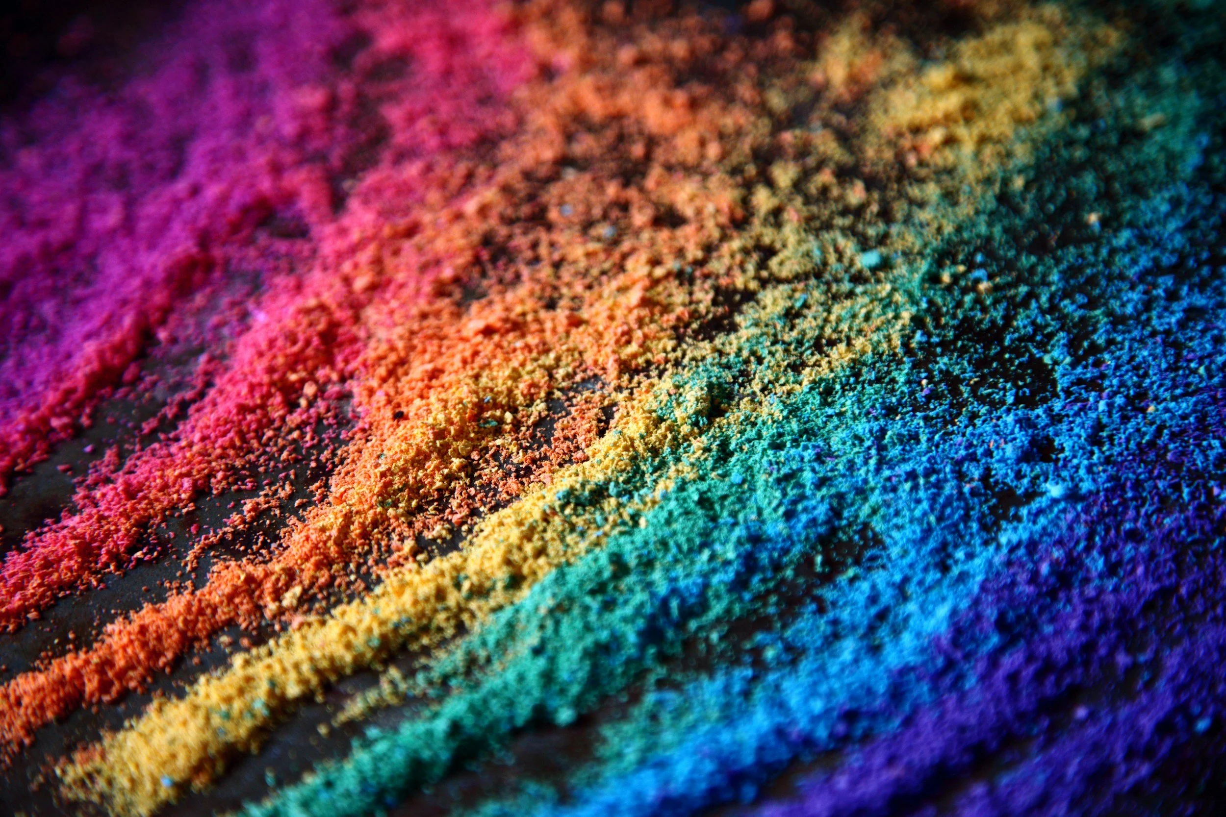 Close-up of colorful enamel powders arranged in rainbow stripes on a dark surface.