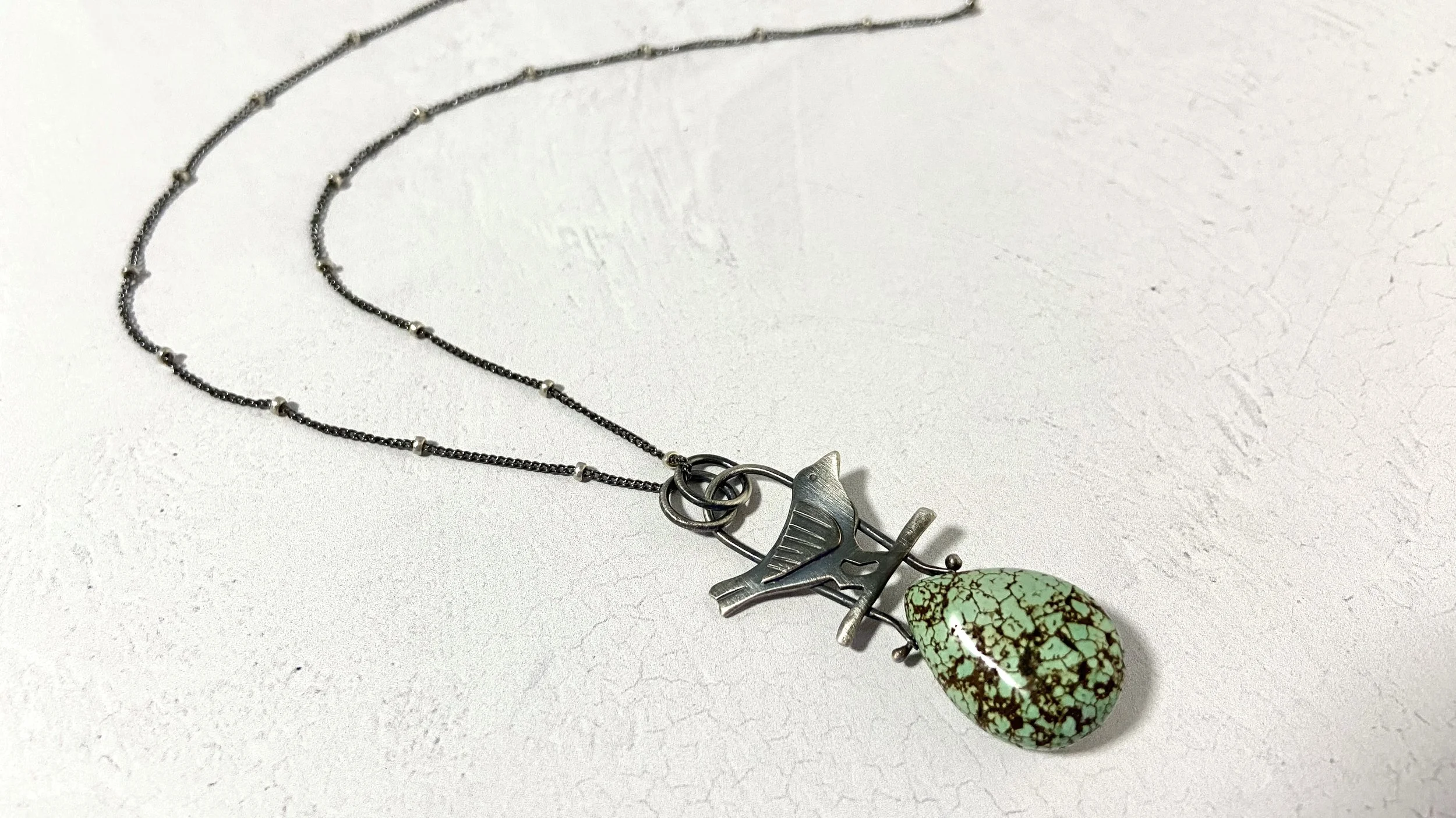 Sterling silver wren necklace sits atop a chunky turquoise pear shaped nugget