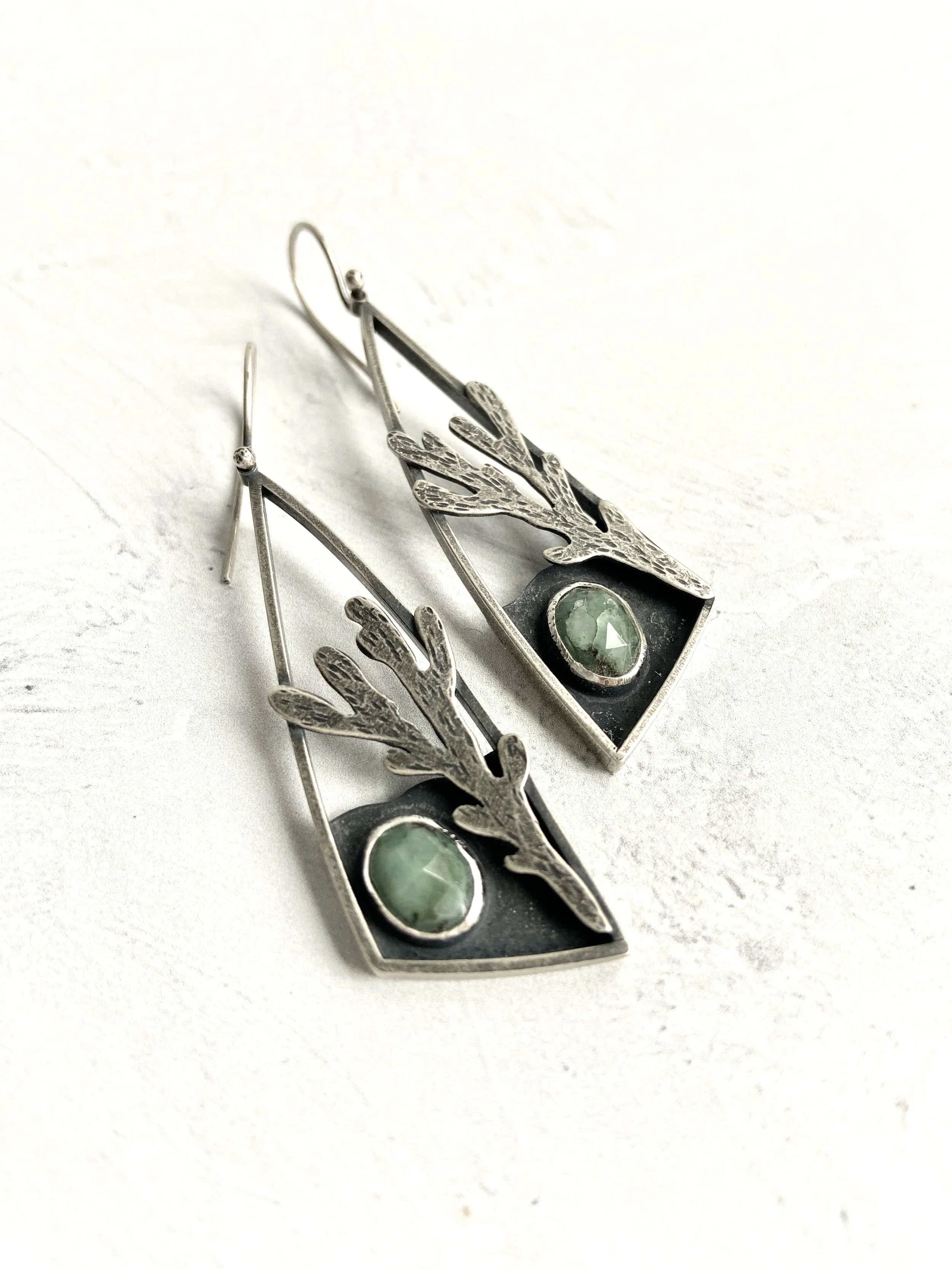 Triangular silver drop earrings with hand sawn and textured silver coral and bezel set emeralds