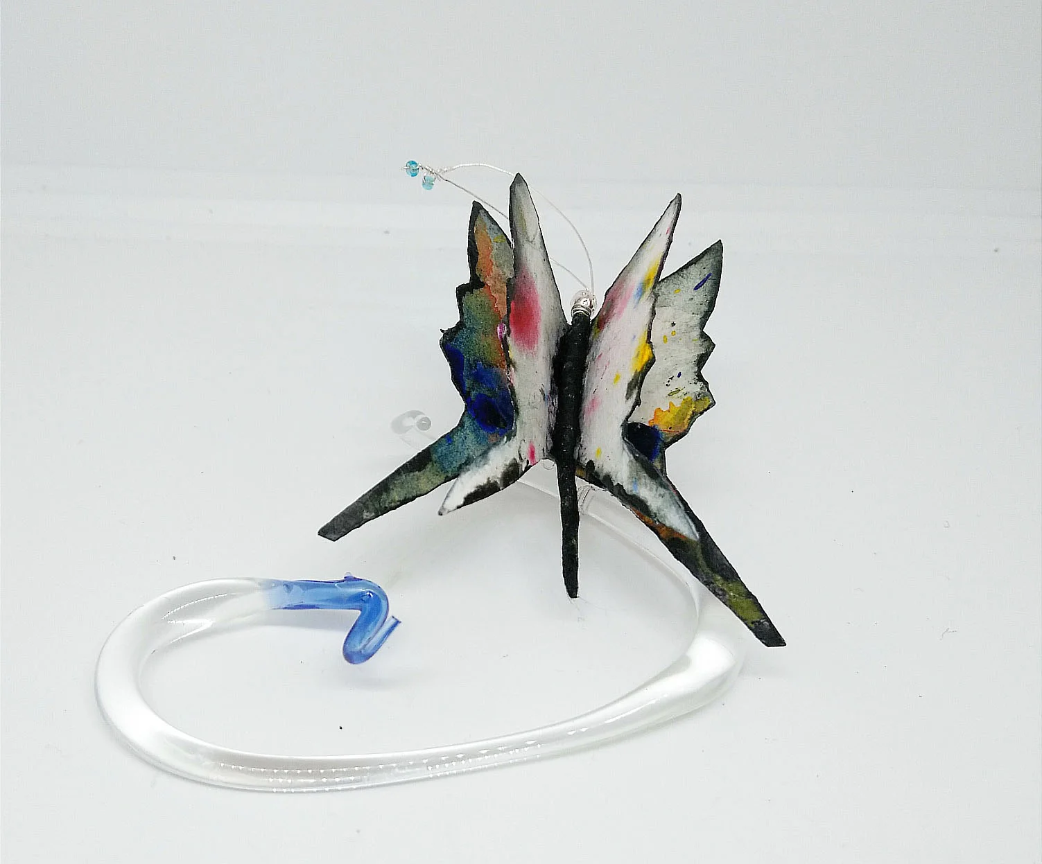 Whisked by A Cloud (view 1) Mixed media borosilicate, clear glass with blue tip, flame work tip and abstract painting on cotton watercolor paper with clear blue glass seed beads at tips of antenna... Appr. L 5 x W 3 1/2 x D 2” Wholesale Price: $95