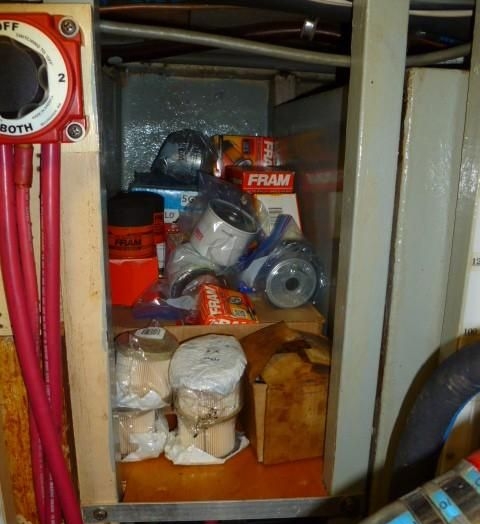 Spare parts and filters and belts get stowed in available space, in this case loose on a shelf. How long before they fall into the bilge when the boat takes a large wake or wave? The sound of things crashing out of lockers and shelves only adds to the anxiety of rough seas.
