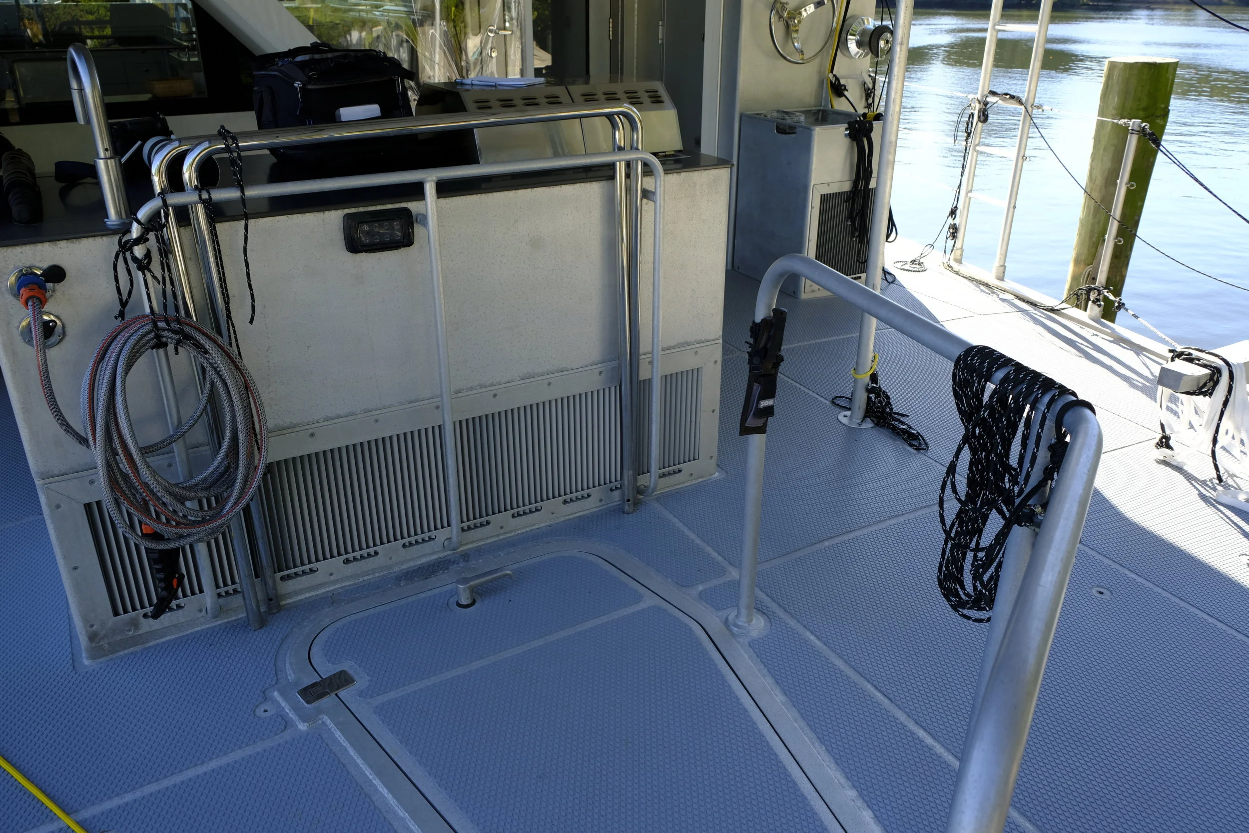 The aluminum structure on the aft cockpit forms the grilling and cooking area, as well as storage for pots and pans to complement the ship's galley. It is a versatile work surface that does duty under way and at anchor. On the backside of this island are large grates that are part of the engine room ventilation. The staples stored here can be installed in the saloon by uncovering plugs in the saloon sole and fitting these hand rails for security at sea if heavy weather is anticipated. The dogged hatch provides access to the aft end of the engine room where the steering and workshop are located.