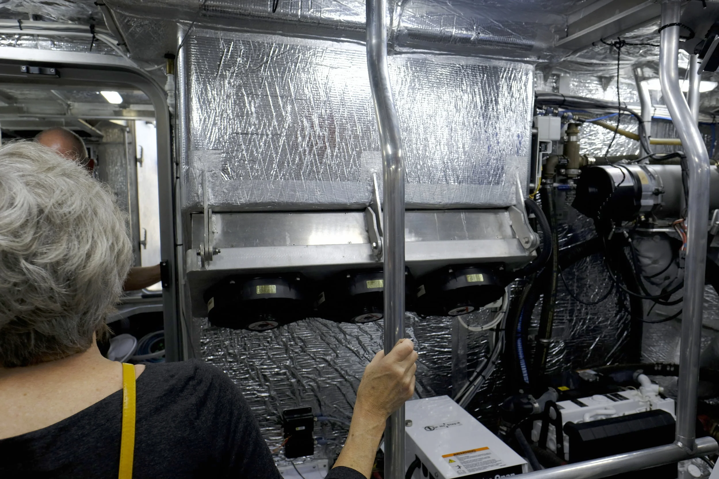 The bottom end of the ventilation structure from the cockpit island enters the aft end of the engine room. Three Delta-T fans pressurize the engine room under way, giving the two Deere diesels plenty of fresh air for maximum performance. In case of electrical or other failure of these high-volume fans, the entire bottom of this ventilation unit swings open (see the three massive hinges on the bottom plate holding the fans), allowing unpressurized air to continue feeding lots of air into the engine room. This is a really well thought out detail and an ideal setup for long distance voyaging.