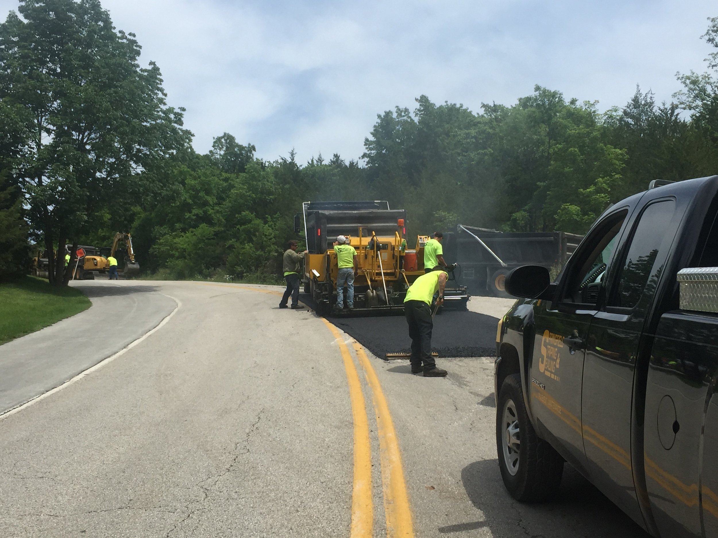 Team of Springfield Striping &amp; Sealing contractors performing asphalt paving and sealing on a curvy road surrounded by greenery near Springfield, MO.