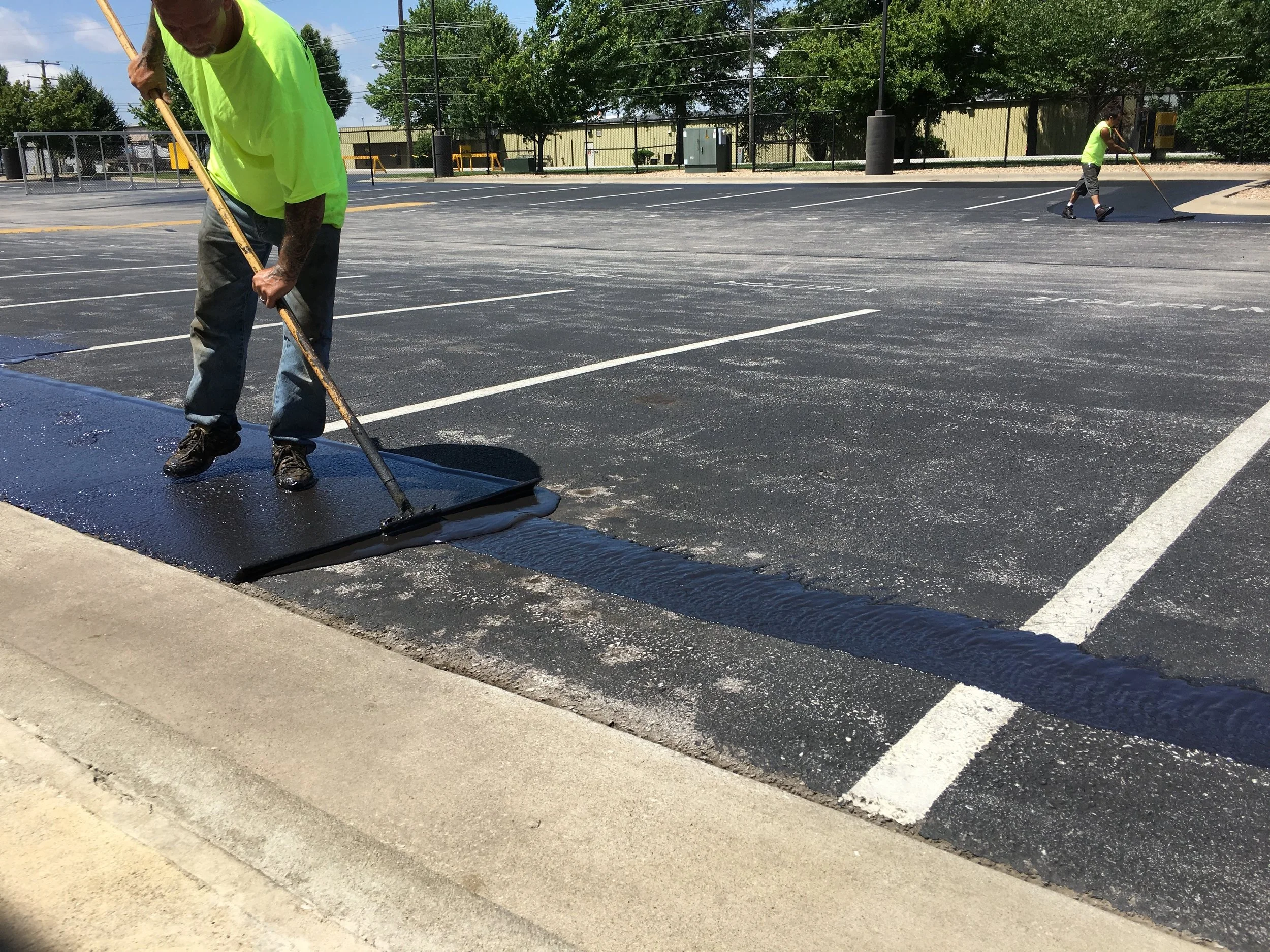 Springfield Striping and Sealing professionals manually coating a parking lot with a push broom asphalt tool in order to increase durability.