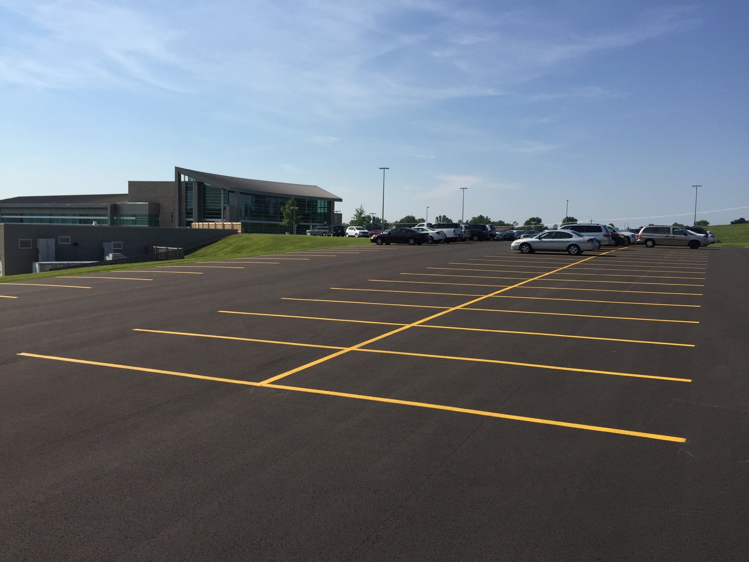 Detailed shot of the line striping process at the OTC parking lot by Springfield Striping and Sealing in Ozark, Missouri, highlighting the precise application of white paint.