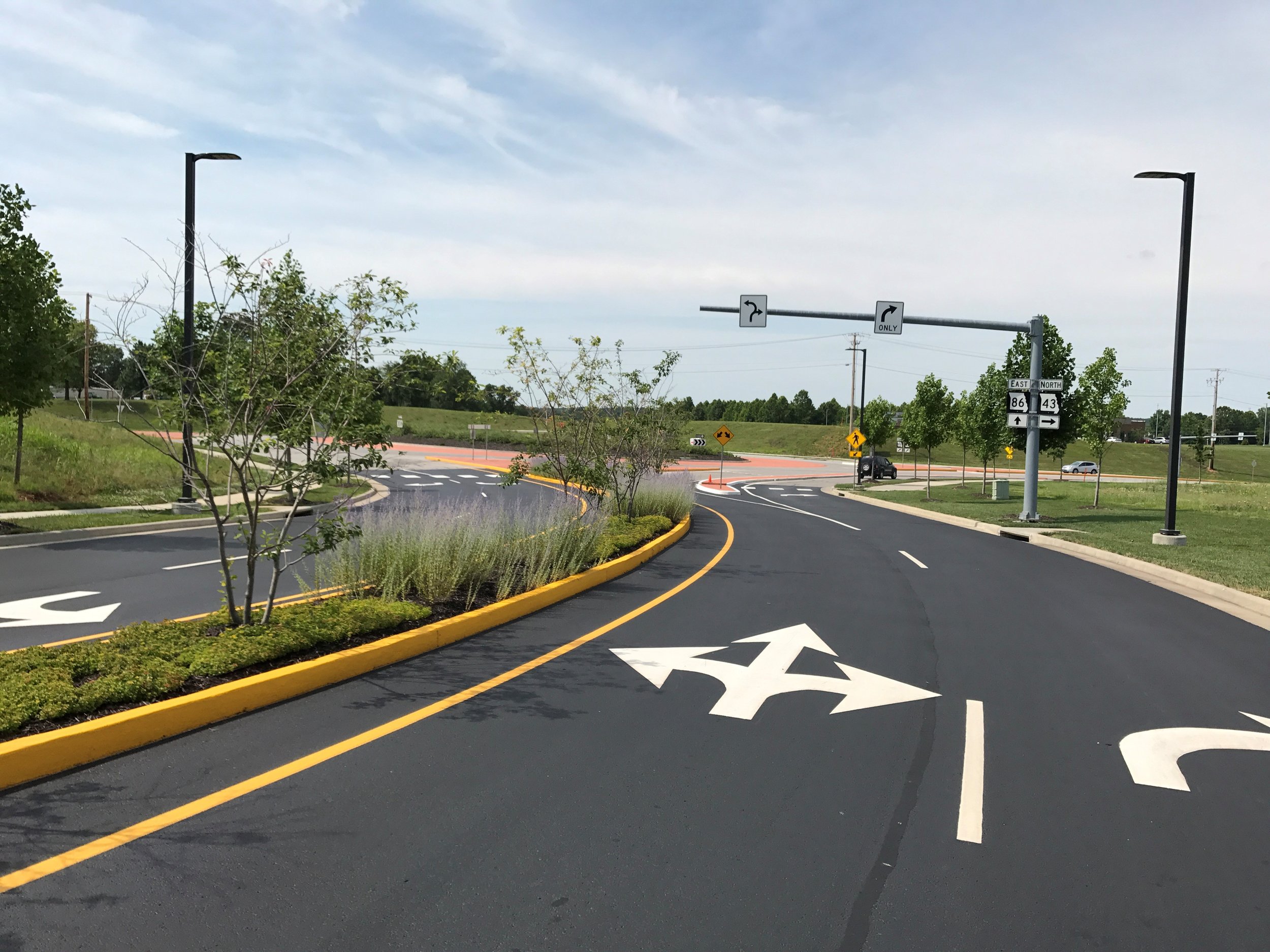 A new intersection with smooth asphalt and road markings by Springfield Striping and Sealing. The intersection features bright yellow curbs and a variety of road arrows.