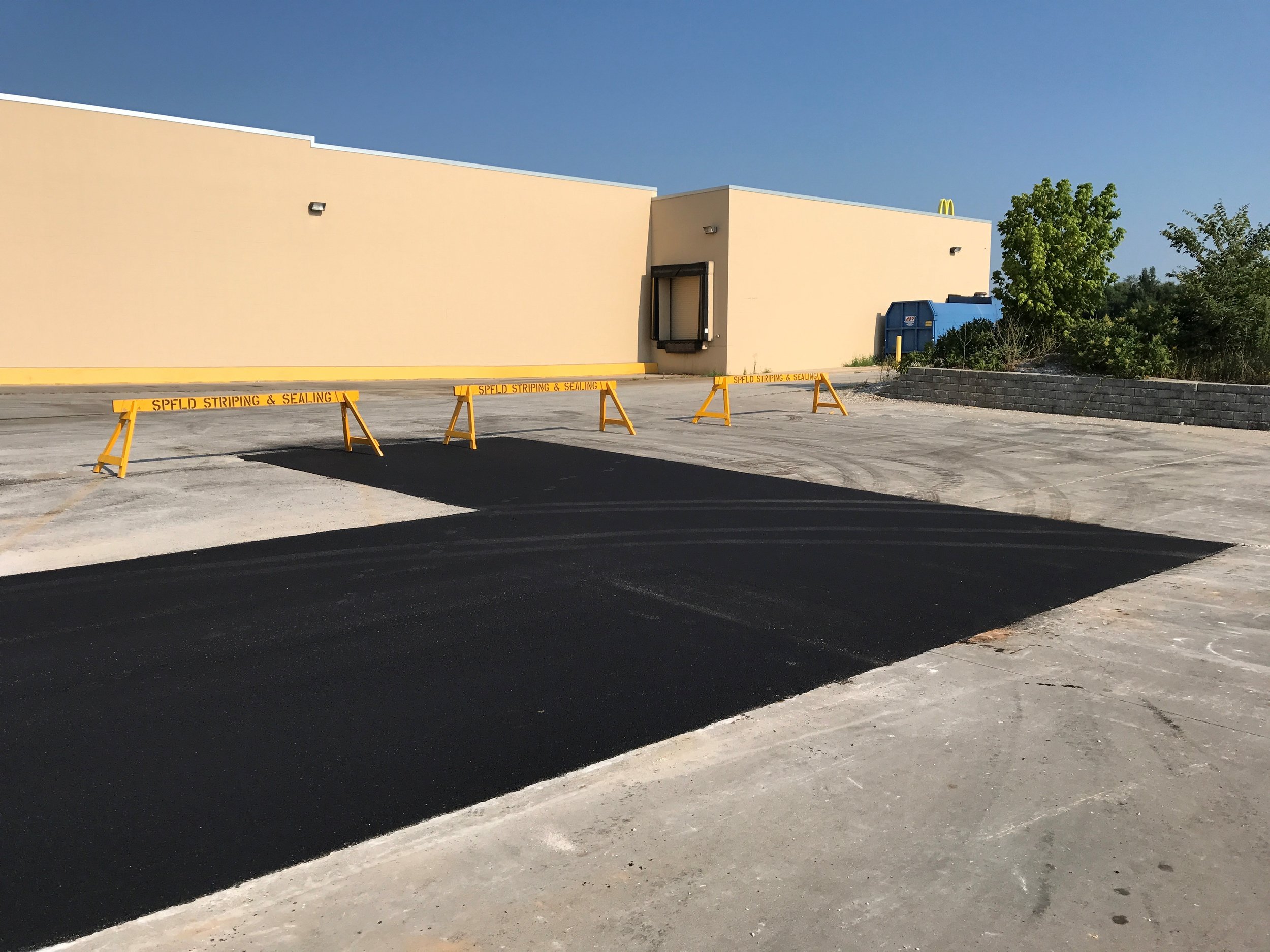 Newly sealcoated section of a parking lot by Springfield Striping &amp; Sealing, sectioned off with safety barriers for drying.