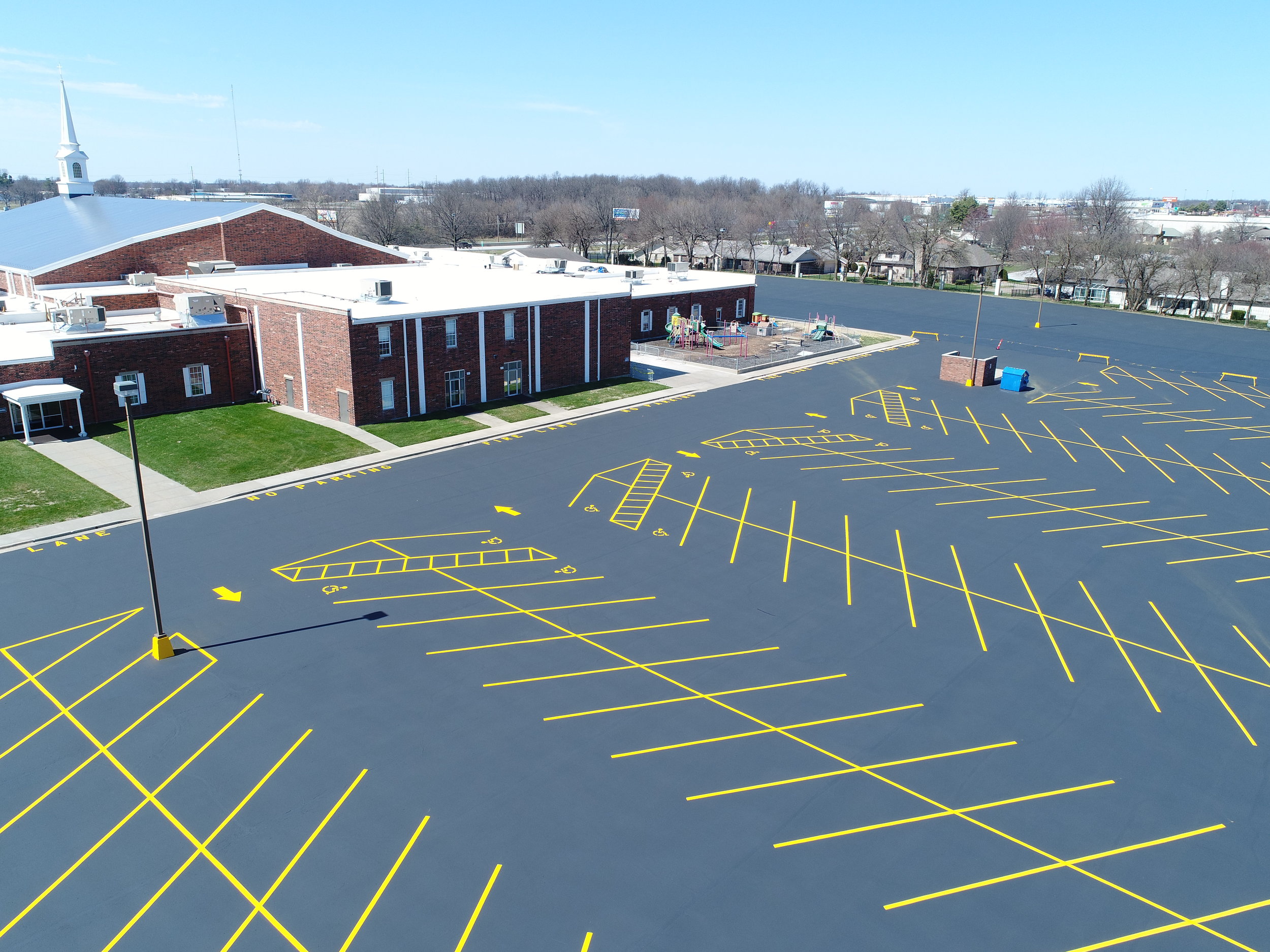 A freshly striped and paved parking lot by Springfield Striping and Sealing at a Springfield, Missouri church, showcasing yellow line striping for parking spaces along with arrows to direct traffic. 