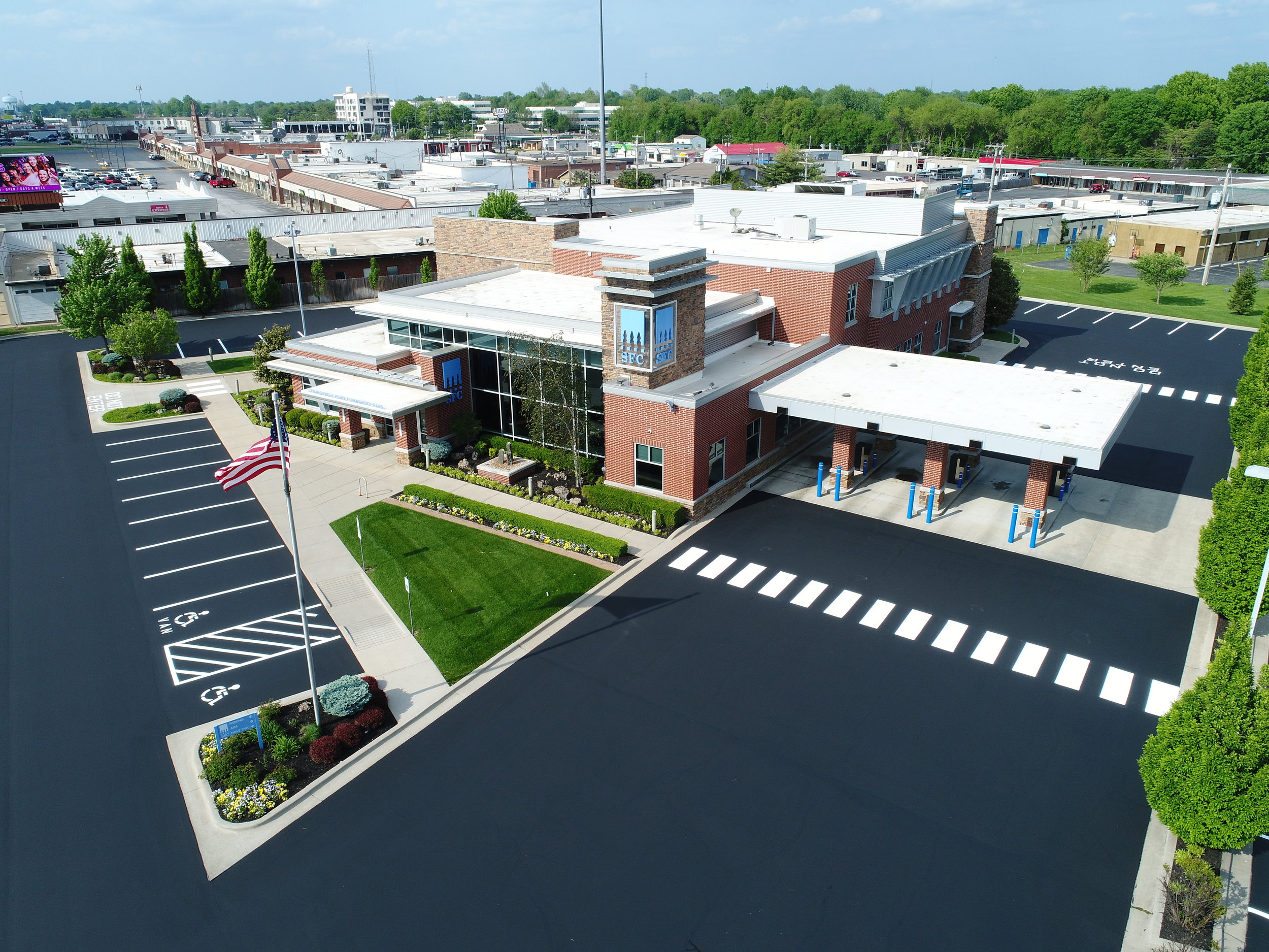 An aerial view displays a commercial building with a newly sealed and striped parking lot done by Springfield Striping and Sealing, complete with landscaping and an American flag, under a clear sky.