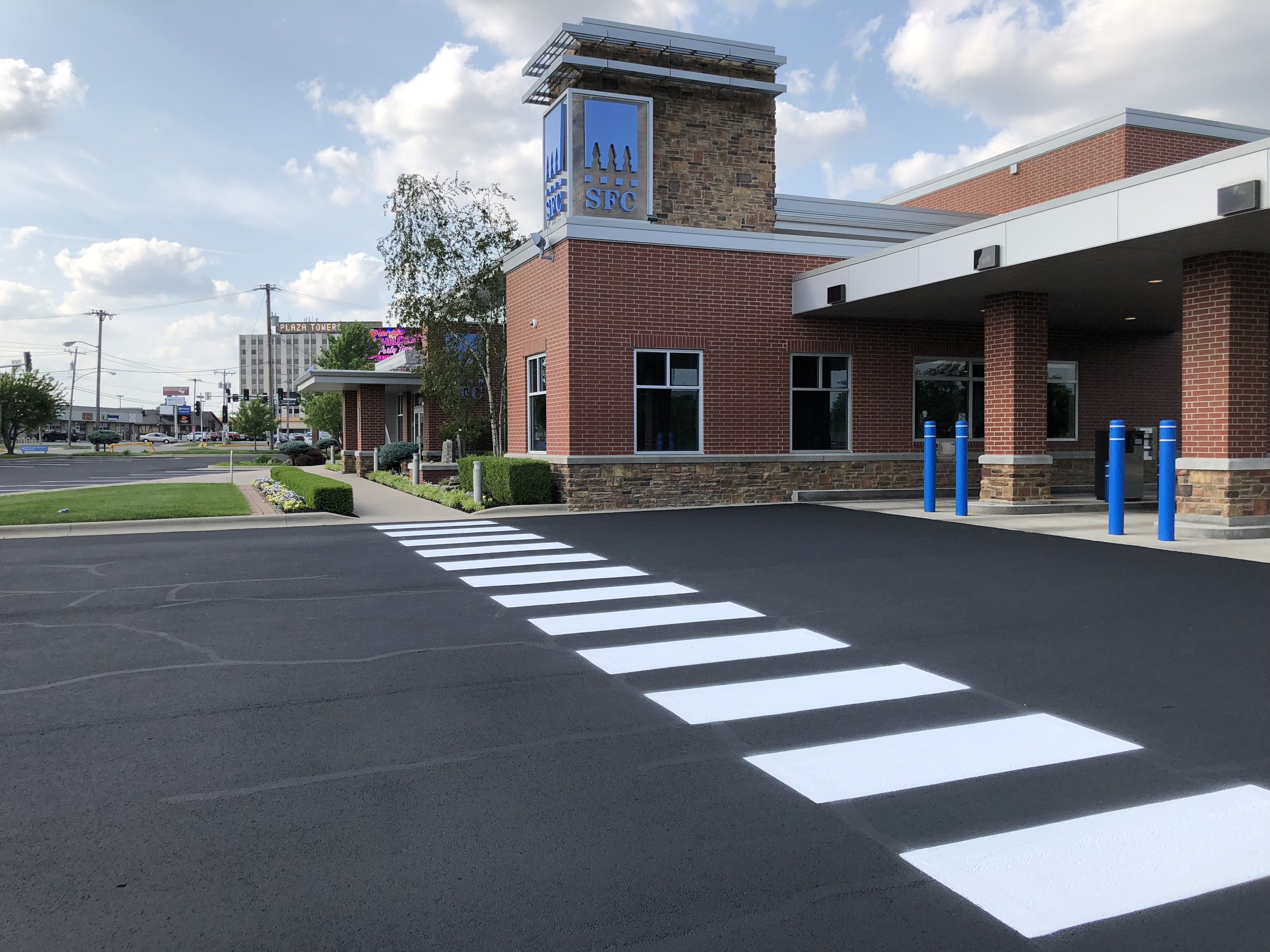 A bank in Springfield Missouri with a clean, freshly striped parking lot featuring white pedestrian crosswalk markings and vibrant blue bollards along the drive-through lane.