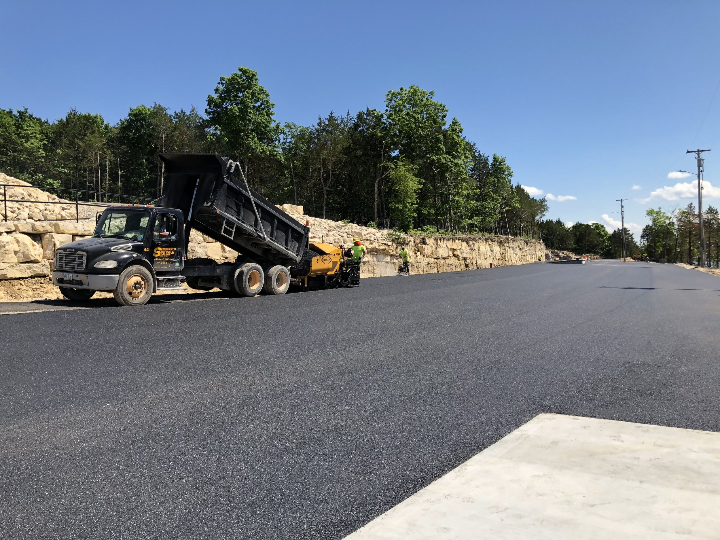 Team performing asphalt paving near Springfield, MO, with a dump truck and paver on a clear day.