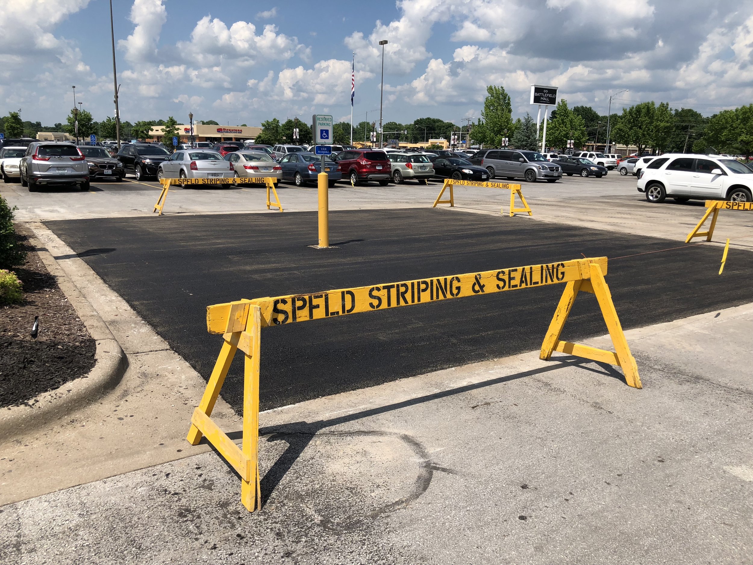 Freshly sealed and striped parking lot area near Springfield, MO, cordoned off with bright yellow Springfield Striping &amp; Sealing barriers.