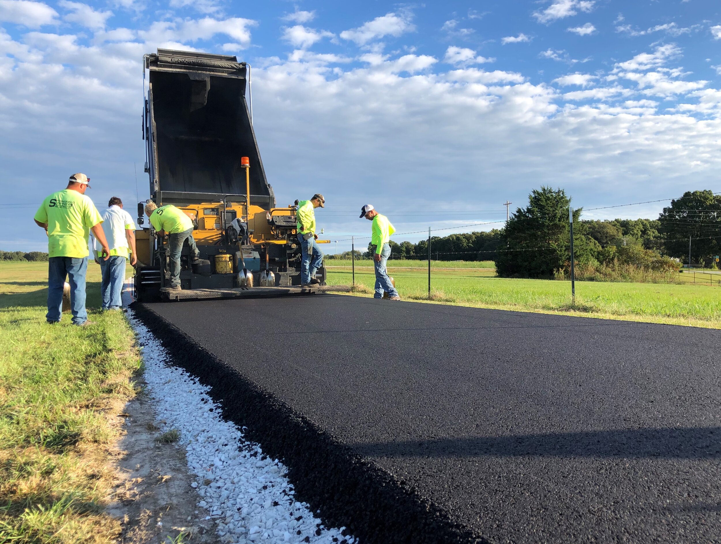 Asphalt paving process near Springfield, MO, with a crew from Springfield Striping &amp; Sealing laying down smooth new pavement.