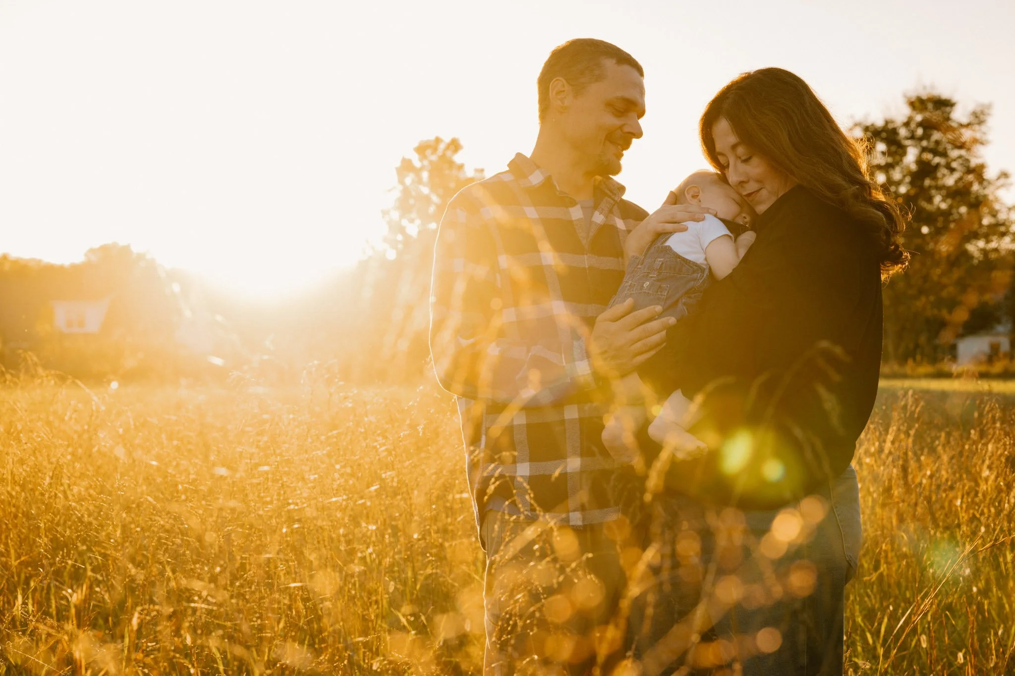 mother and father snuggling their baby with golden sunlight