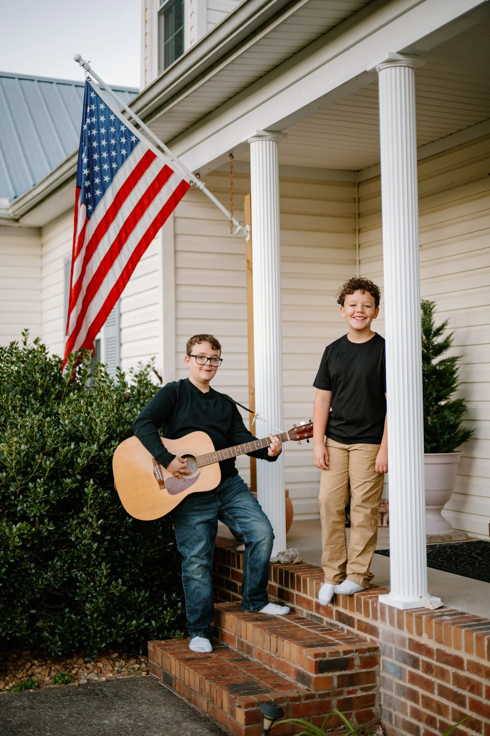 portrait of two boys on the front steps of a home with a guitar and american flage