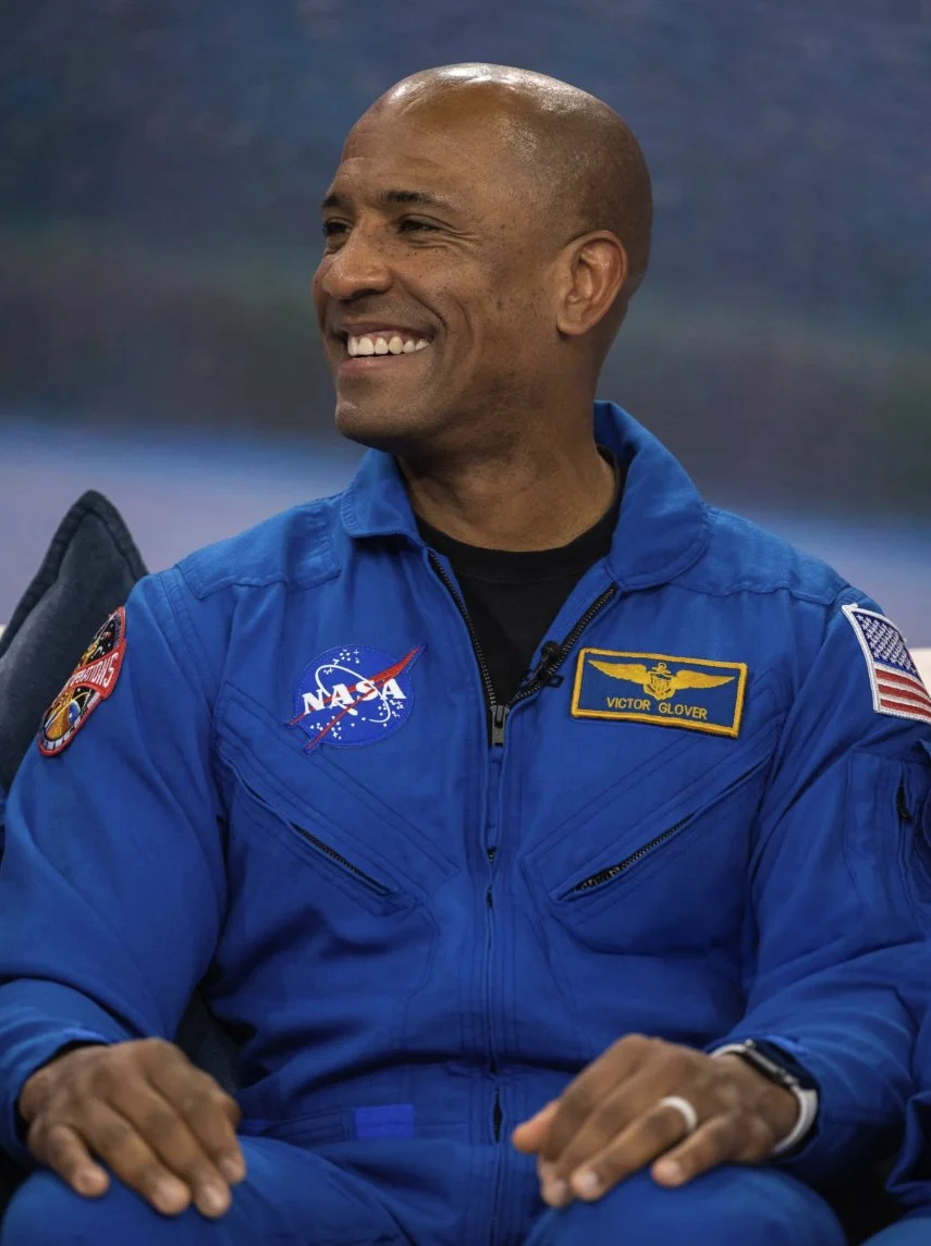 NASA astronaut Victor Glover in a royal-blue flight suit with mission patches and a name tag: reference for the uniform color and patch placement.