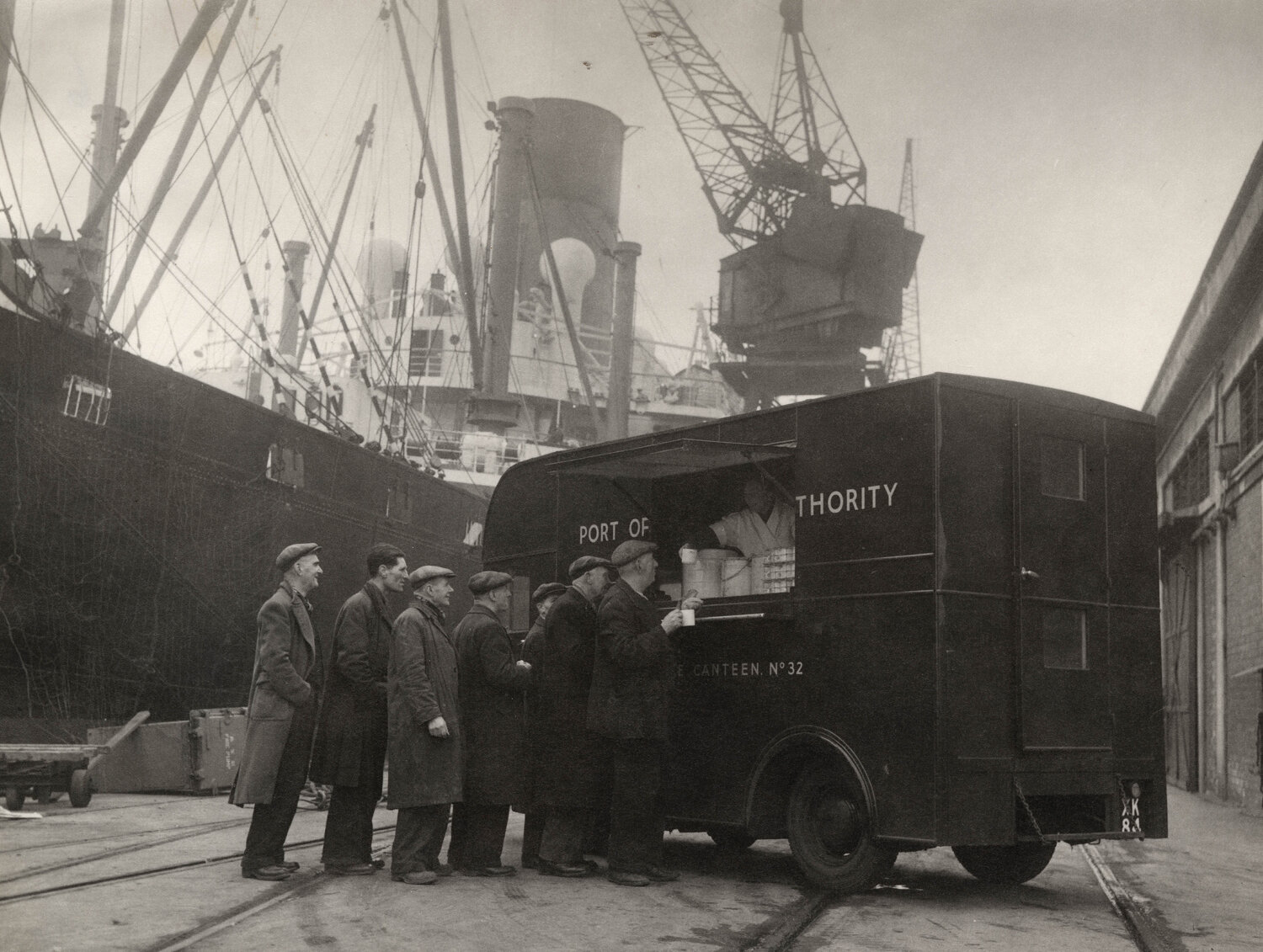 Staff of the Port of London’s Mobile Canteen No.32 dispense tea to queuing dockers, 1942