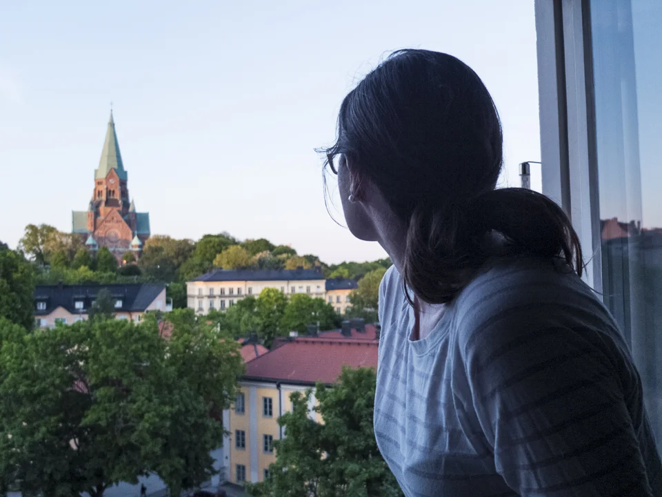 My wife enjoying the view of Sofia Kyrka in Nytorget through our apartment window during a long summer evening in Stockholm.