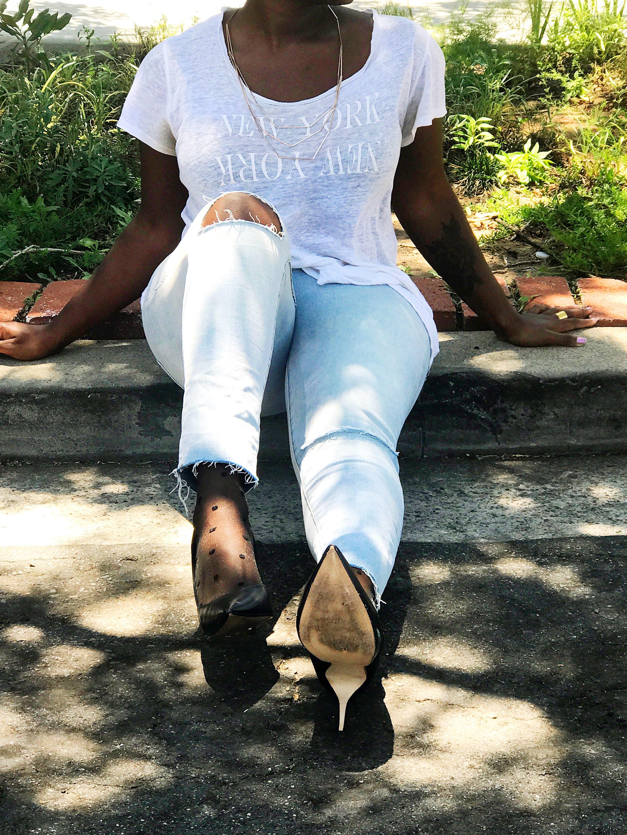 Woman sitting on curb wearing Madewell t-shirt, Urban Outfitters ripped jeans, and black pumps
