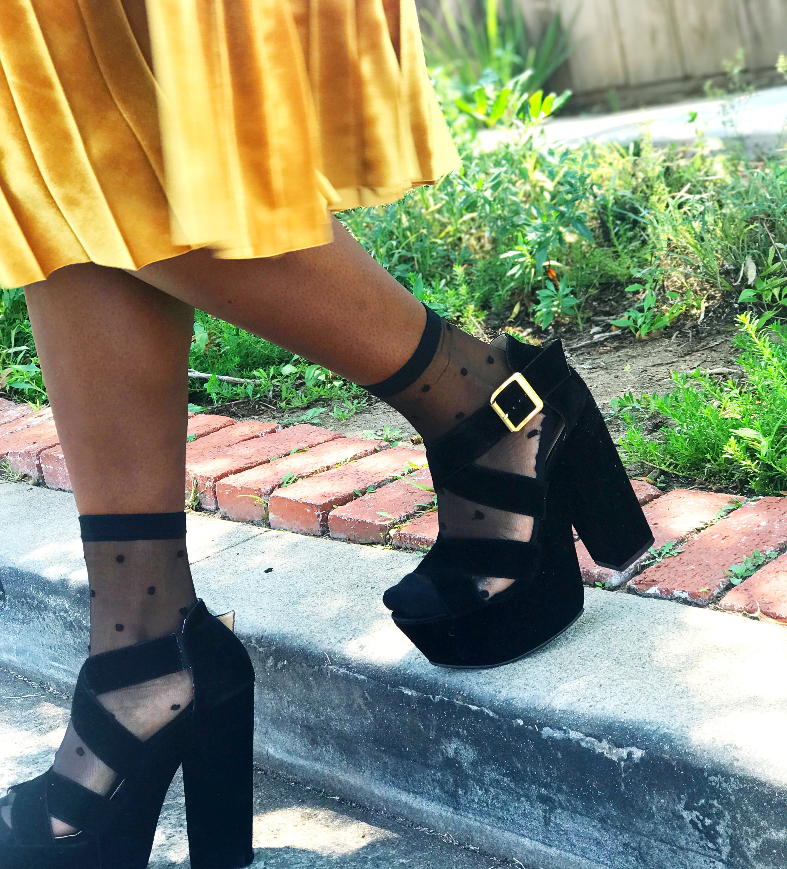 Black woman stepping off curb wearing chunky heels, sheer socks, gold pleated velvet skirt #streetstyle