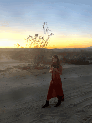Sarah Natsumi Moore, Austin commercial photographer, walking through Joshua Tree desert in a rust red dress — behind the scenes BTS