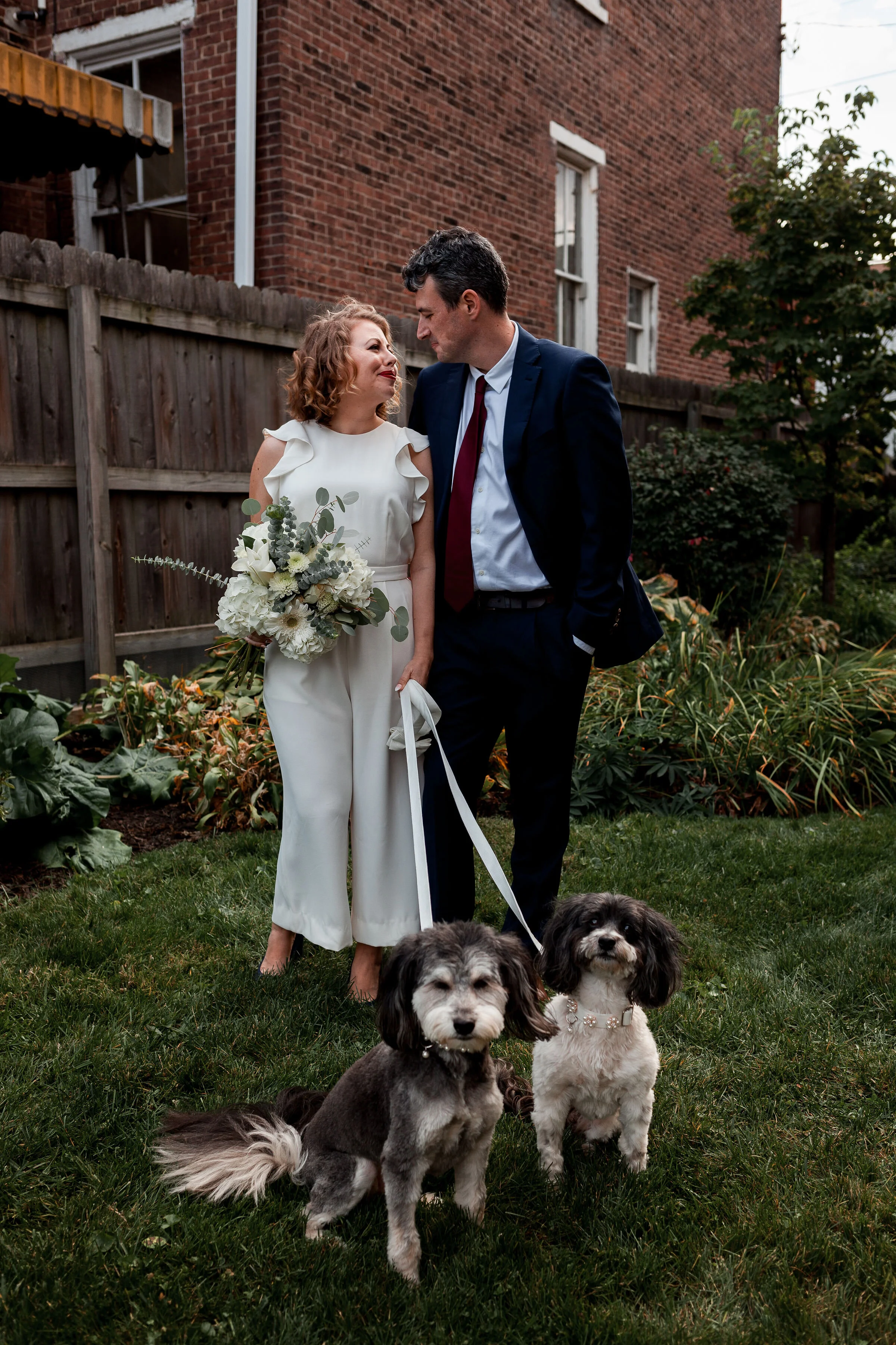 Bride and groom standing with their dogs in backyard in Pittsburgh.