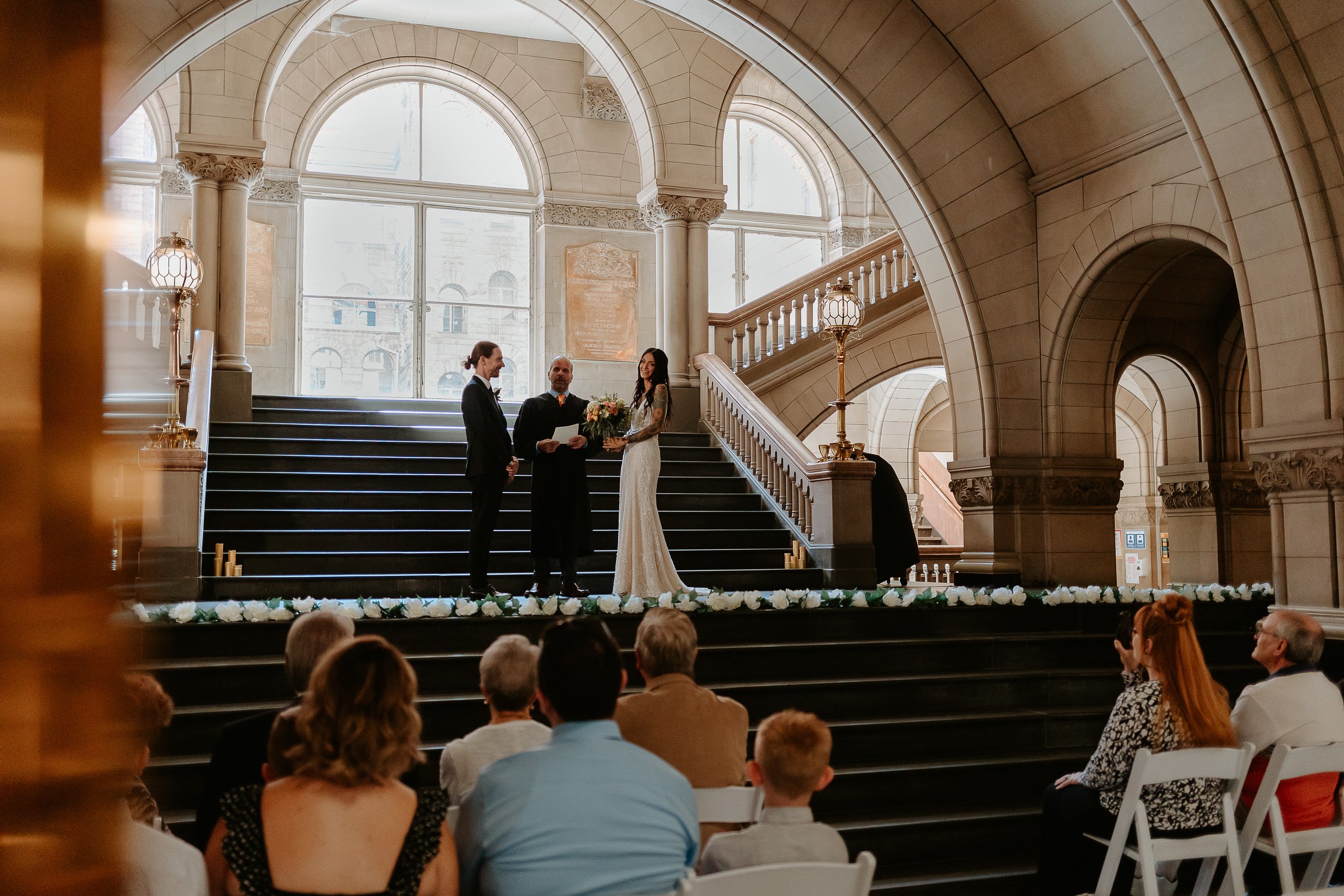 Bride and groom stand on stairs of courthouse during ceremony.