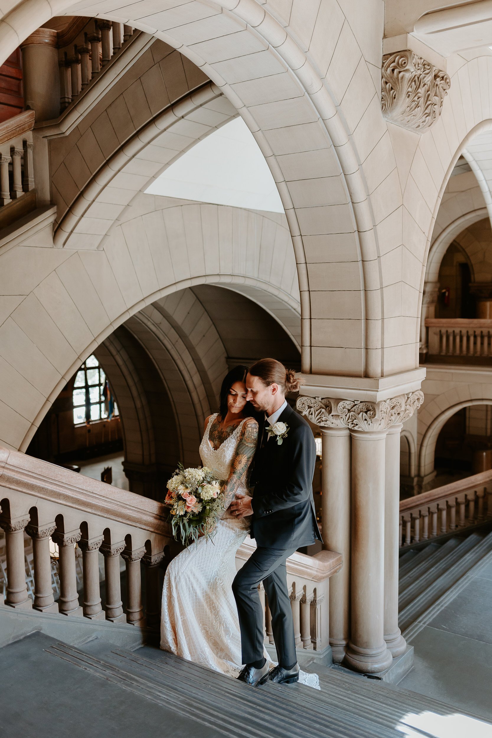 Bride and groom stand on stairs, embracing each other at courthouse.