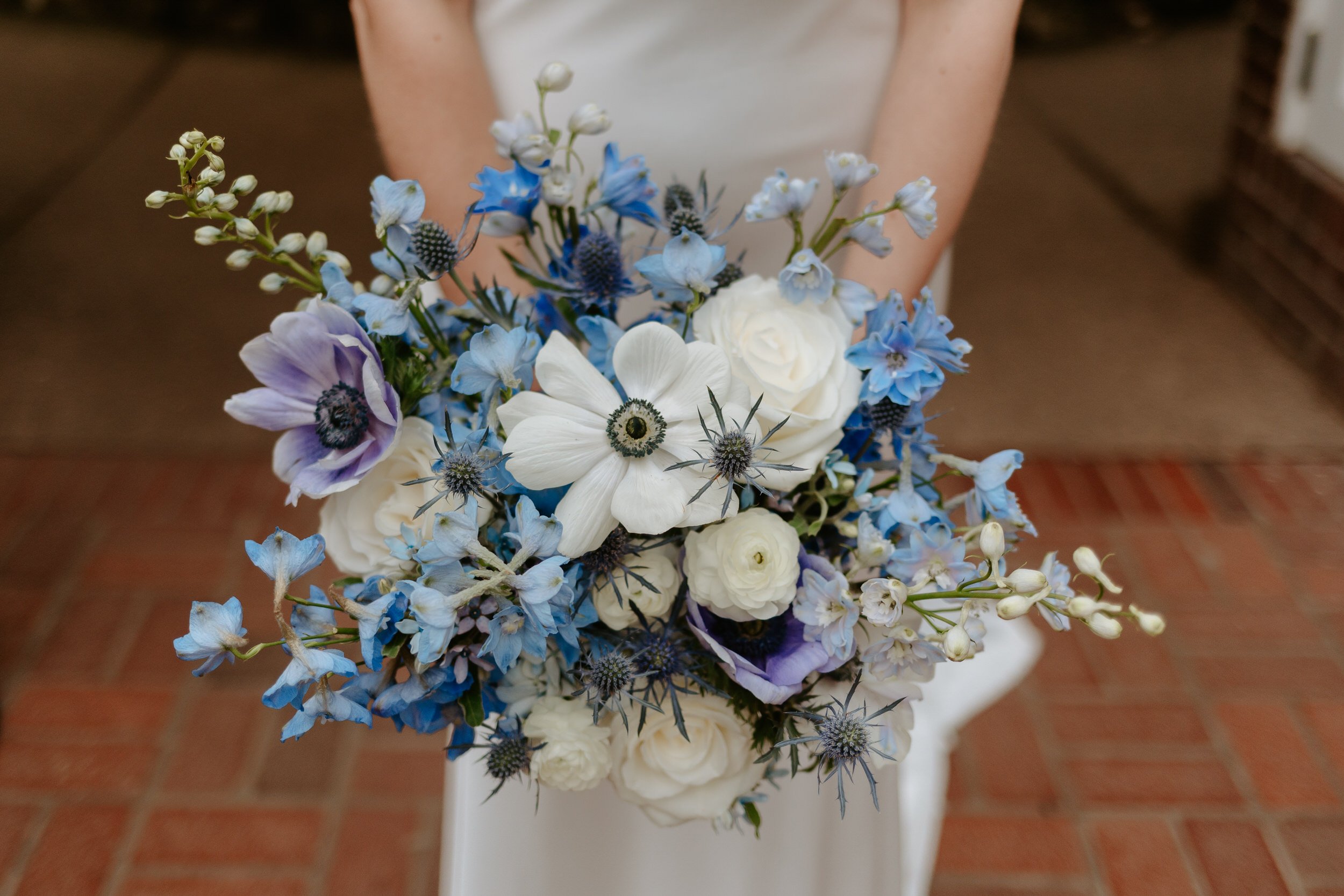  Bride holds blue toned bouquet to show it’s details. 