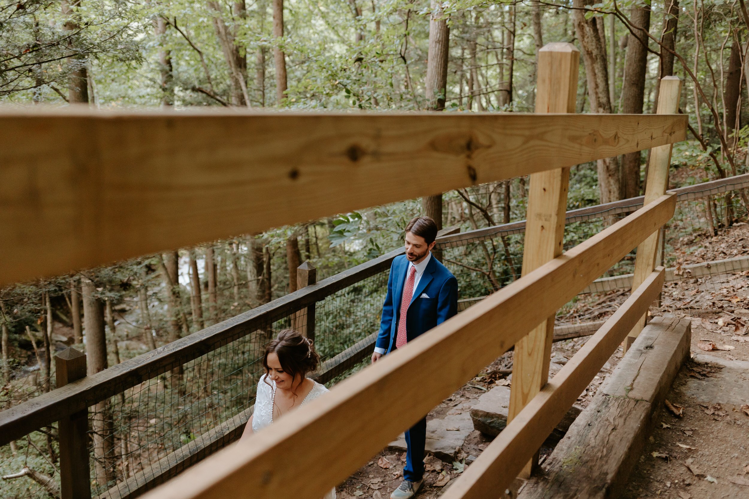 Couple in wedding attire makes their way down a trail path.