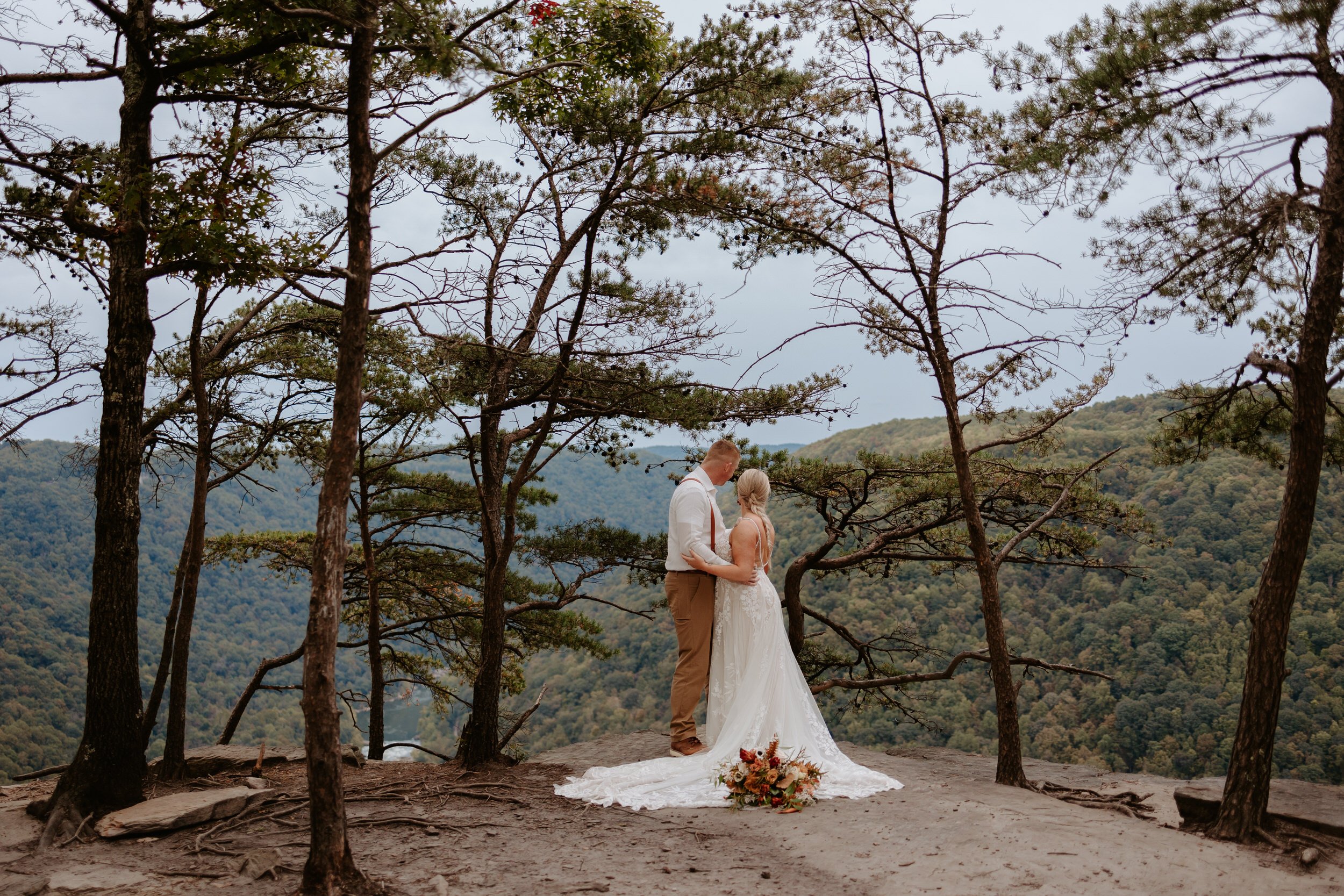 Bride and groom embrace on cliff at New River Gorge.