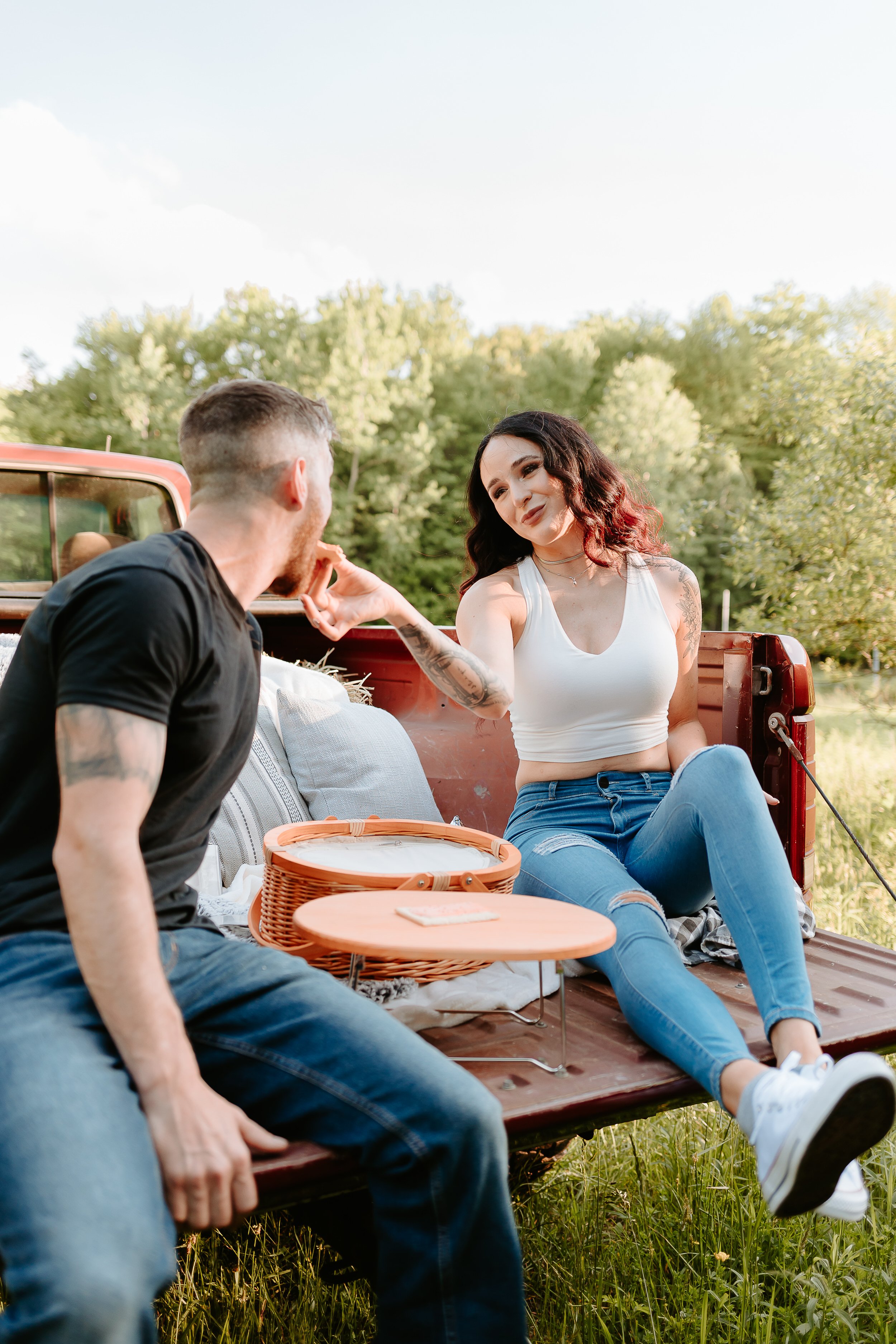 Couple shares a bite to eat in the bed of a red truck.