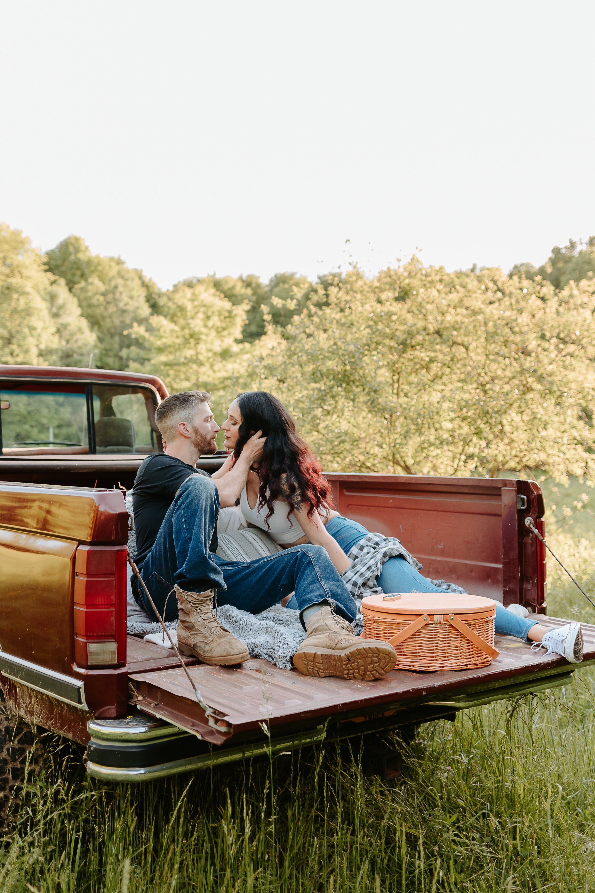 Woman leans into man to kiss while sitting in bed of red truck.