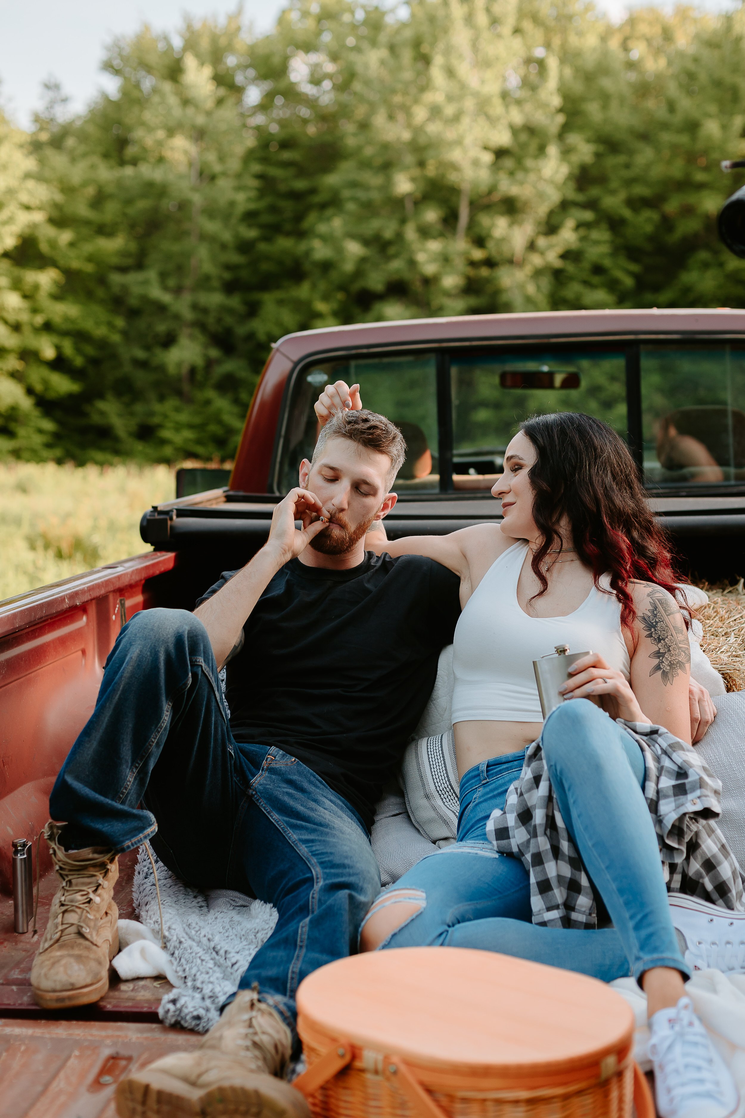 Man smokes joint while woman sits next to him in the bed of a truck.