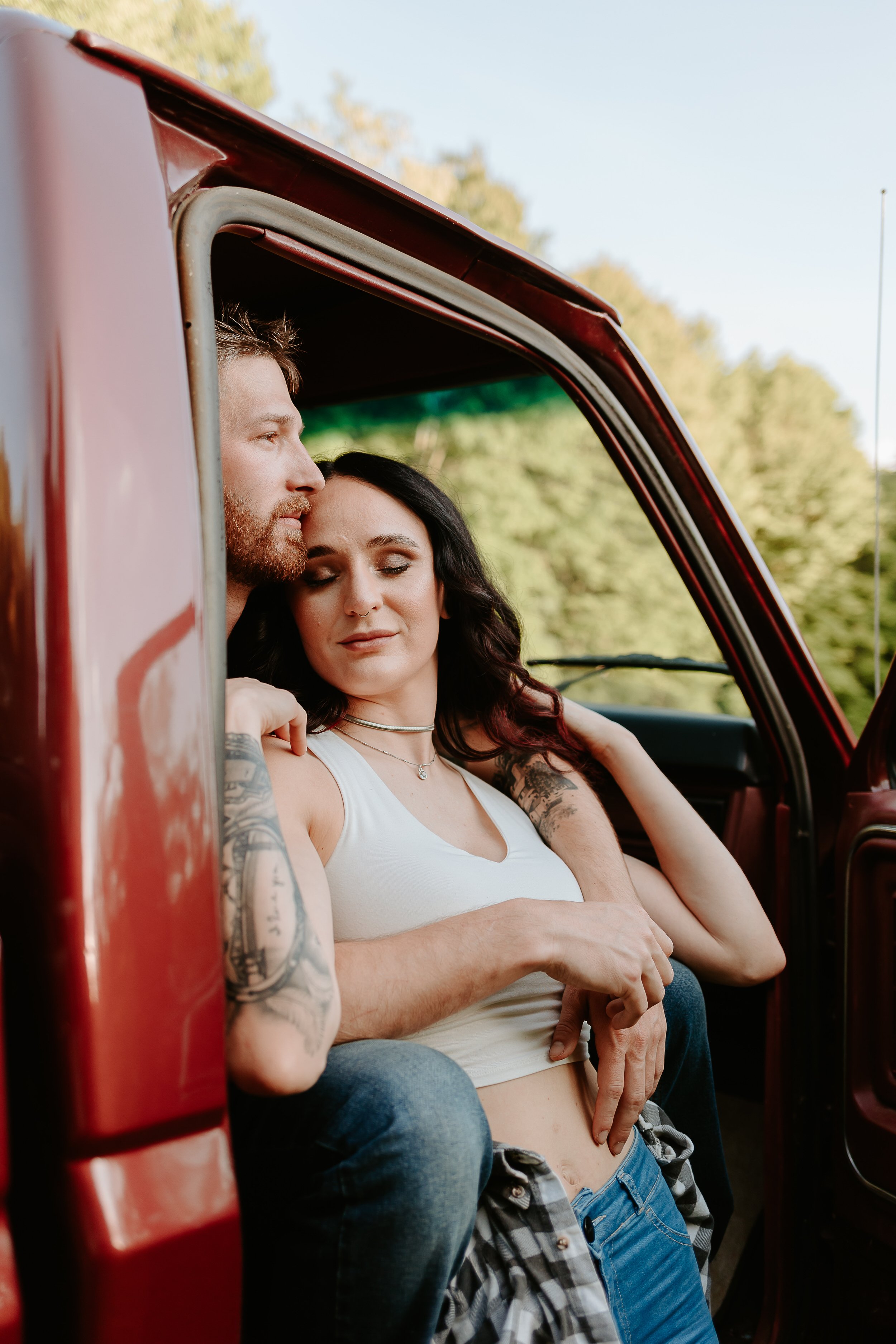 Man holds fiancé while sitting in red truck.