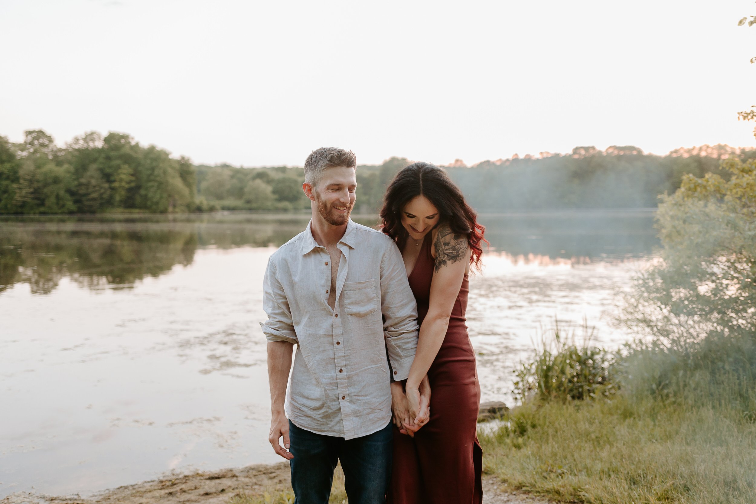 Man and fiancé laughing in front of a lake.