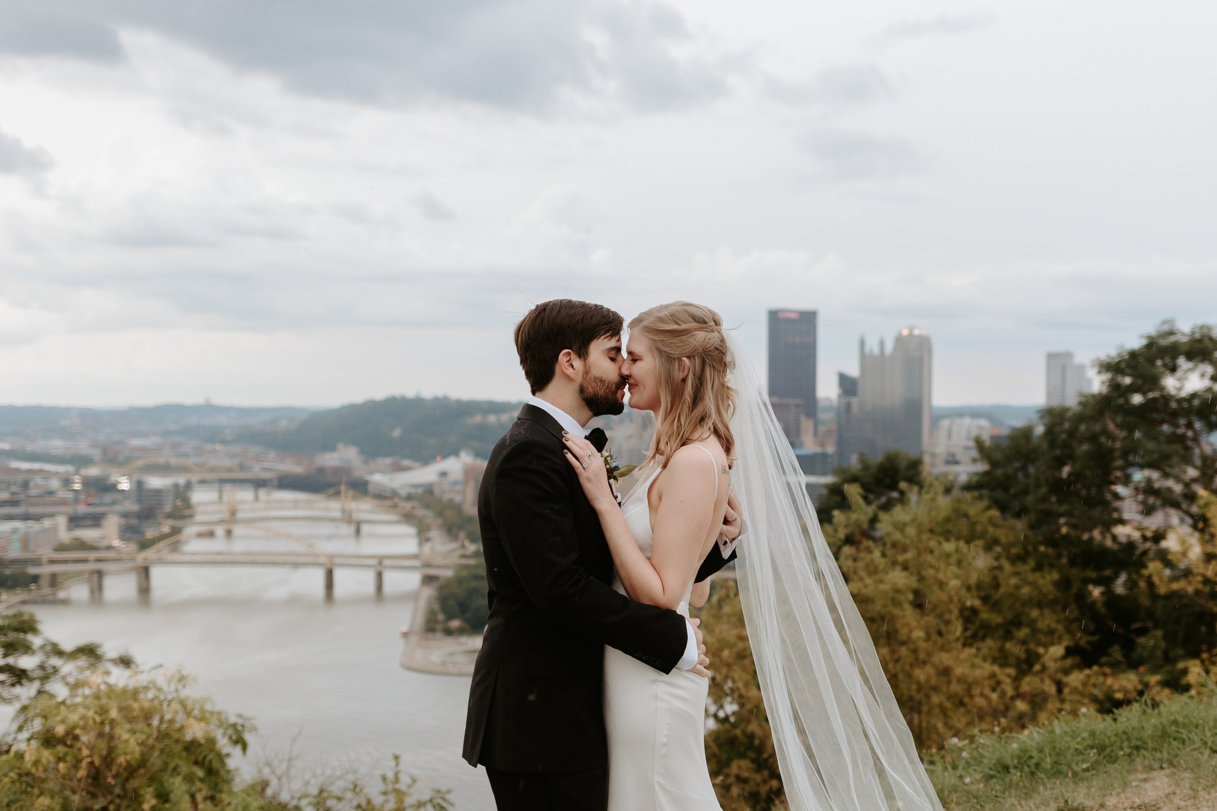 Bride and groom face each other with city skyline in the background.
