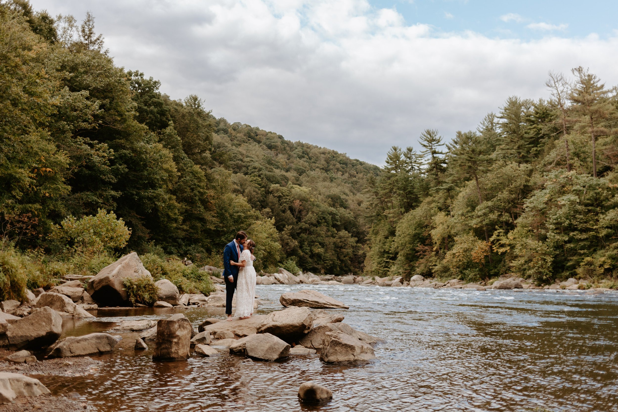 Couple kissing on rock on the edge of a river.