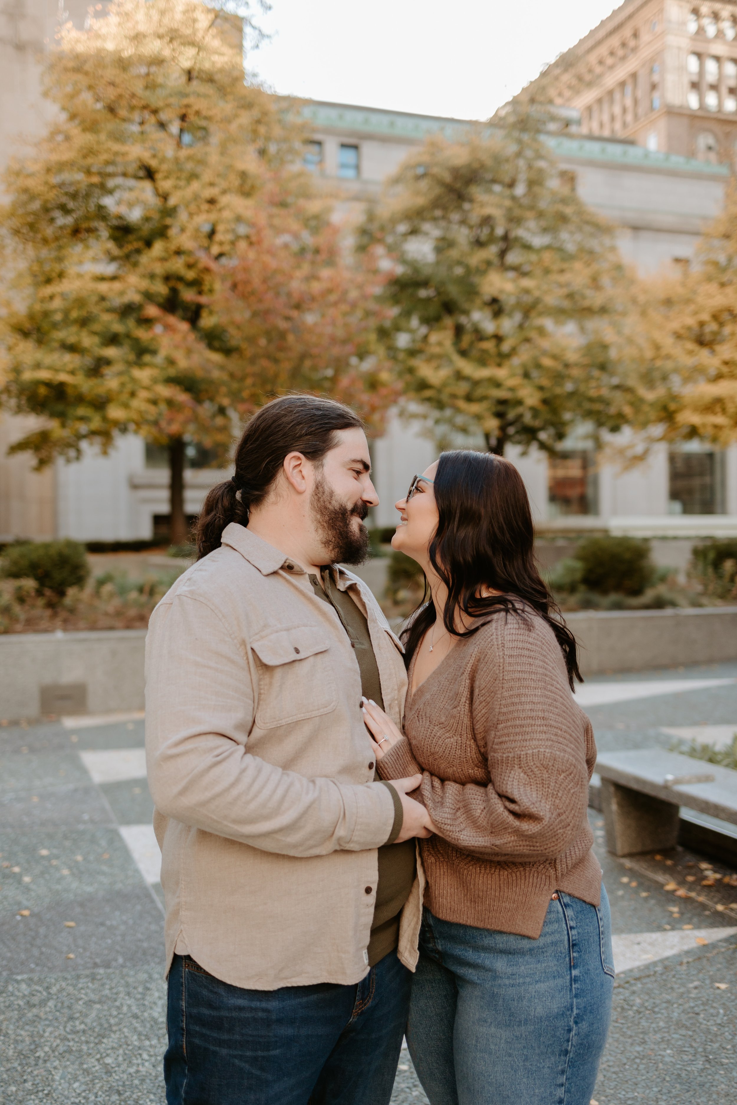 Couple looking at each other with fall colored trees around them.