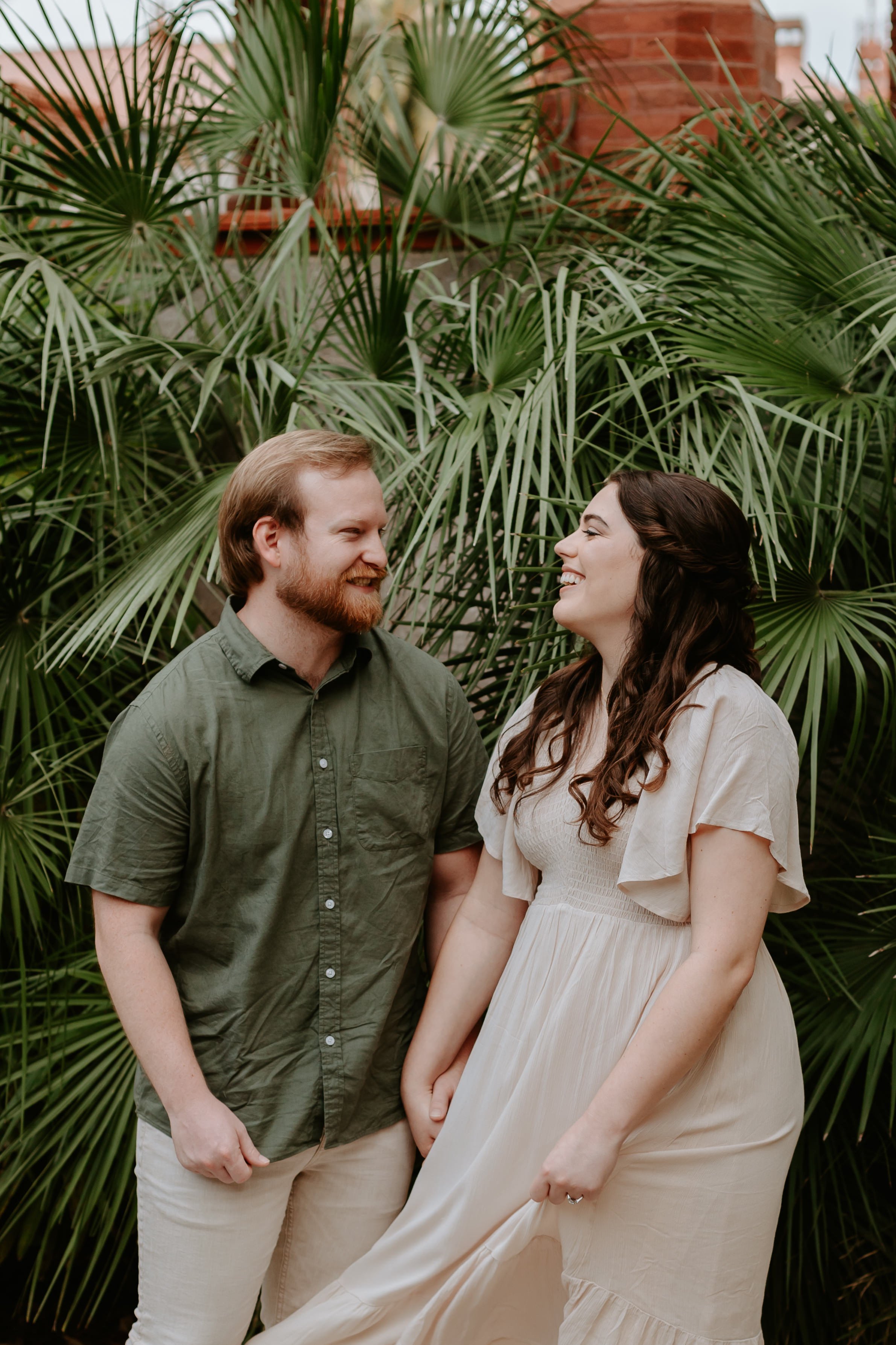 Man and woman smile at each other in front of palm fronds.