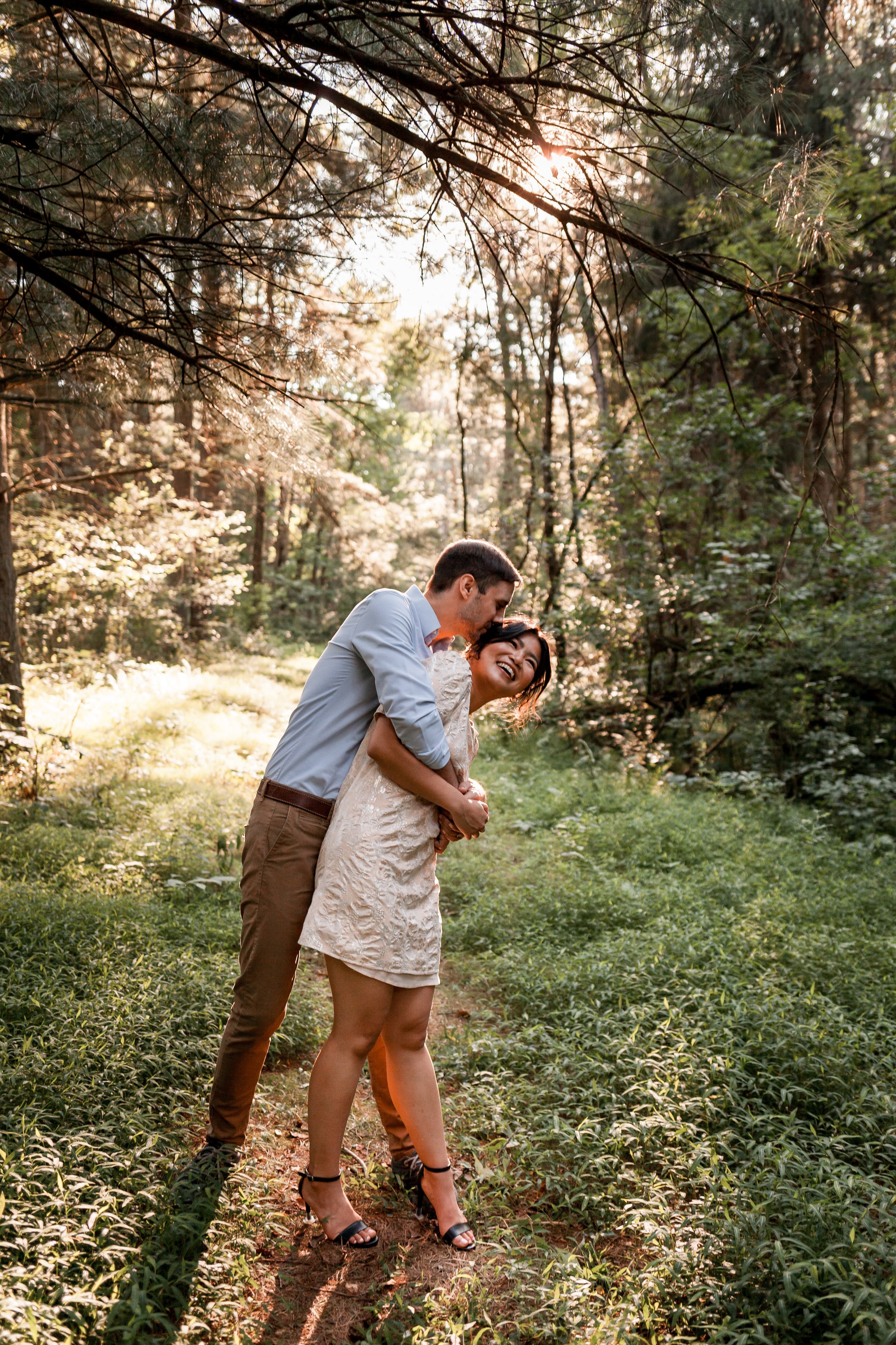 A man and woman hugging in the woods.