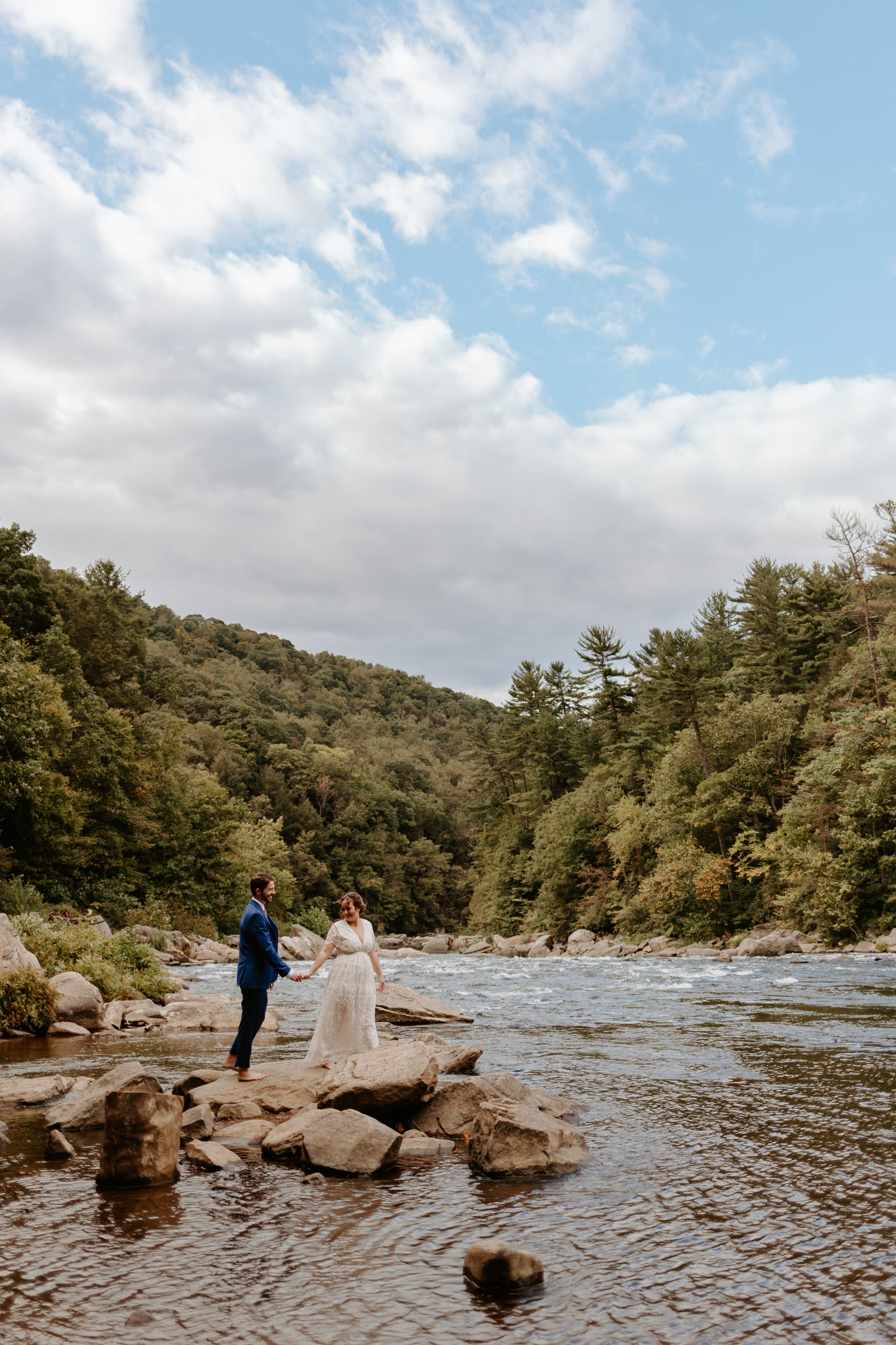 A bride and groom standing on rocks in a river.