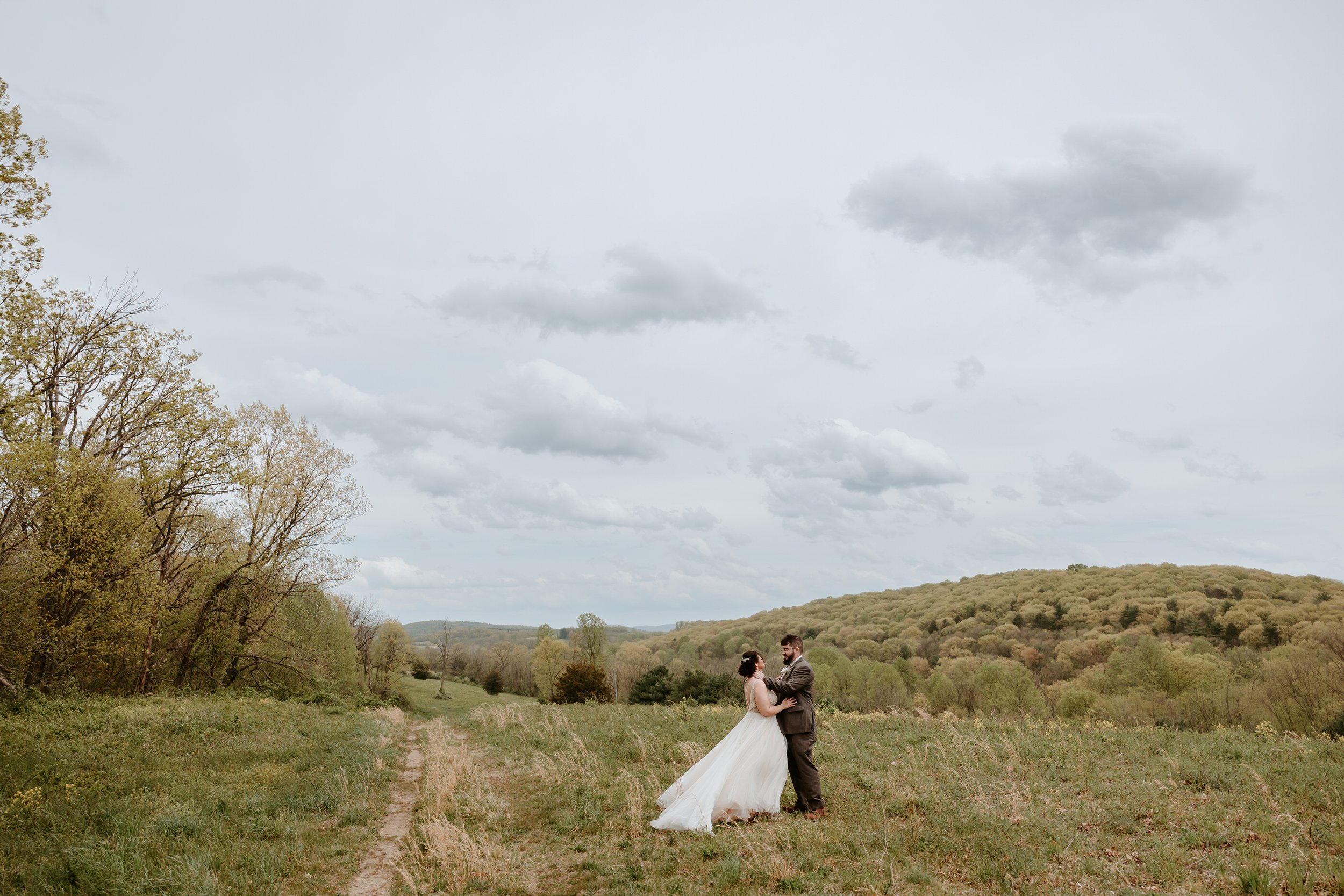 Bride and groom embrace on top of hill with mountain in the background.