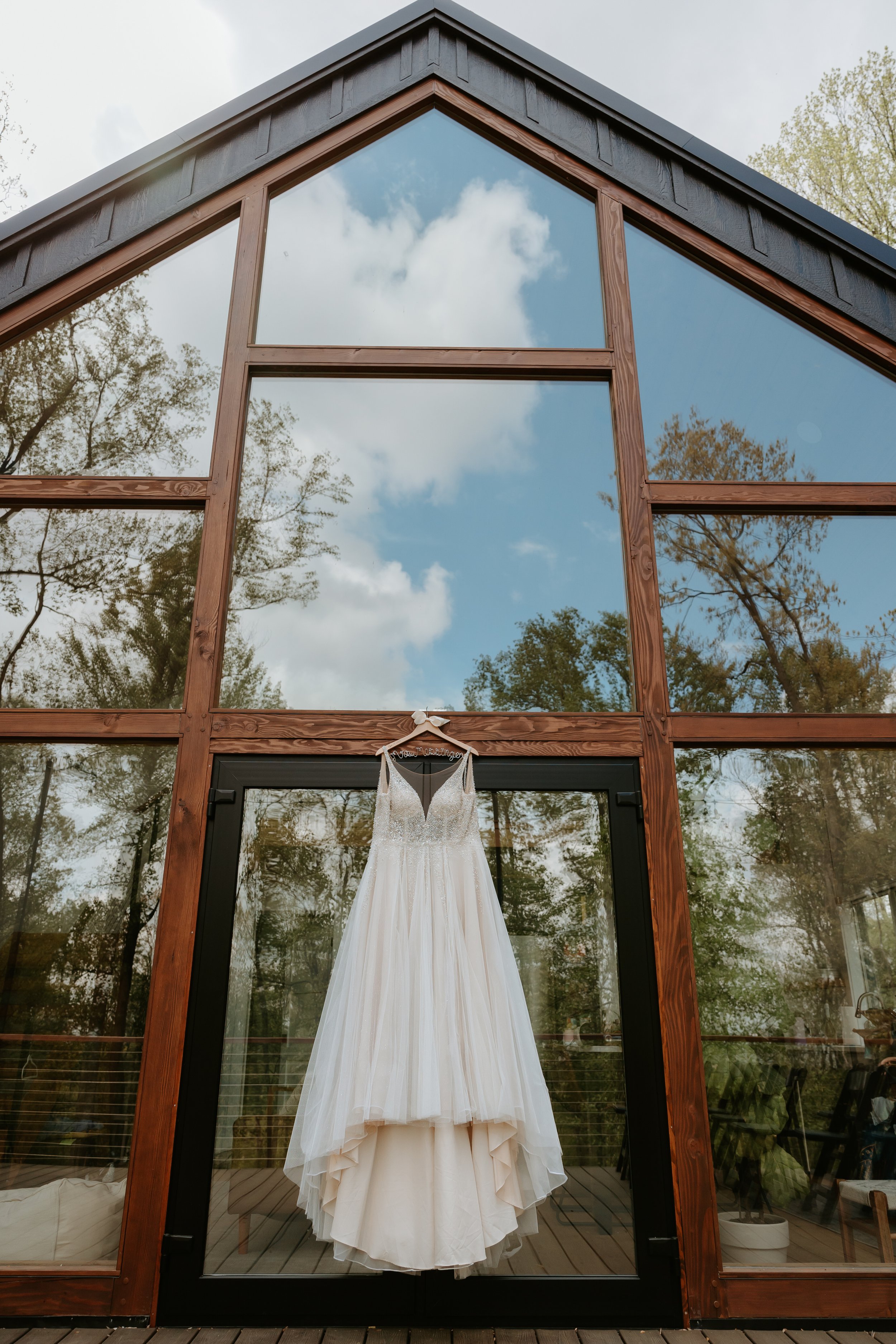 Wedding dress hangs in front of large two story window.