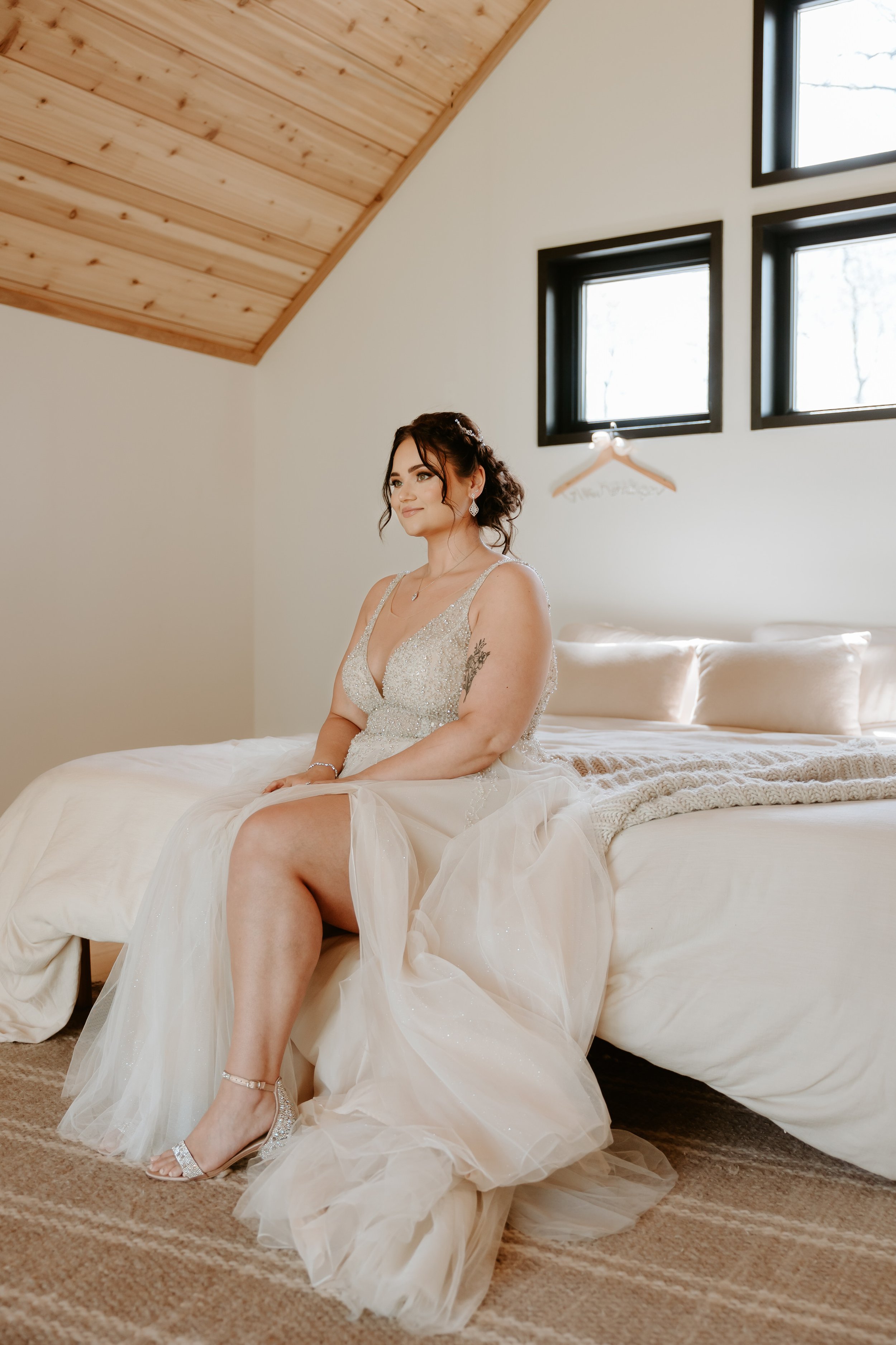 Bride sits on edge of bed and smiles. 